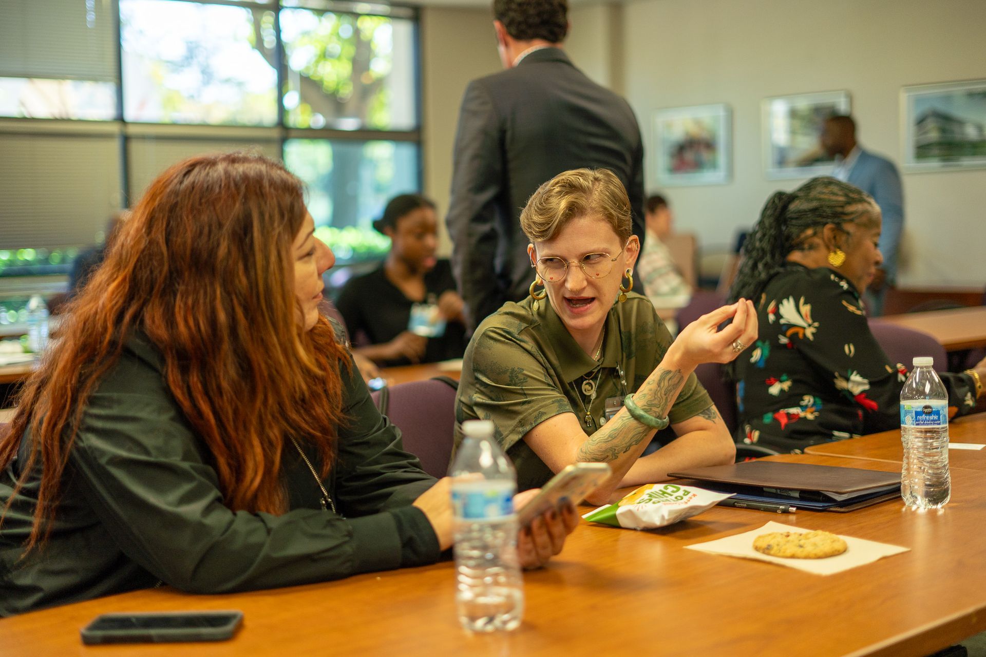 People talking at a conference table with water bottles and snacks in a bright meeting room