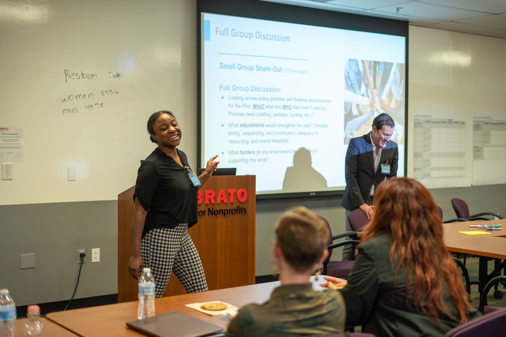 Presenter speaking beside projected slides in a classroom while students watch and take notes