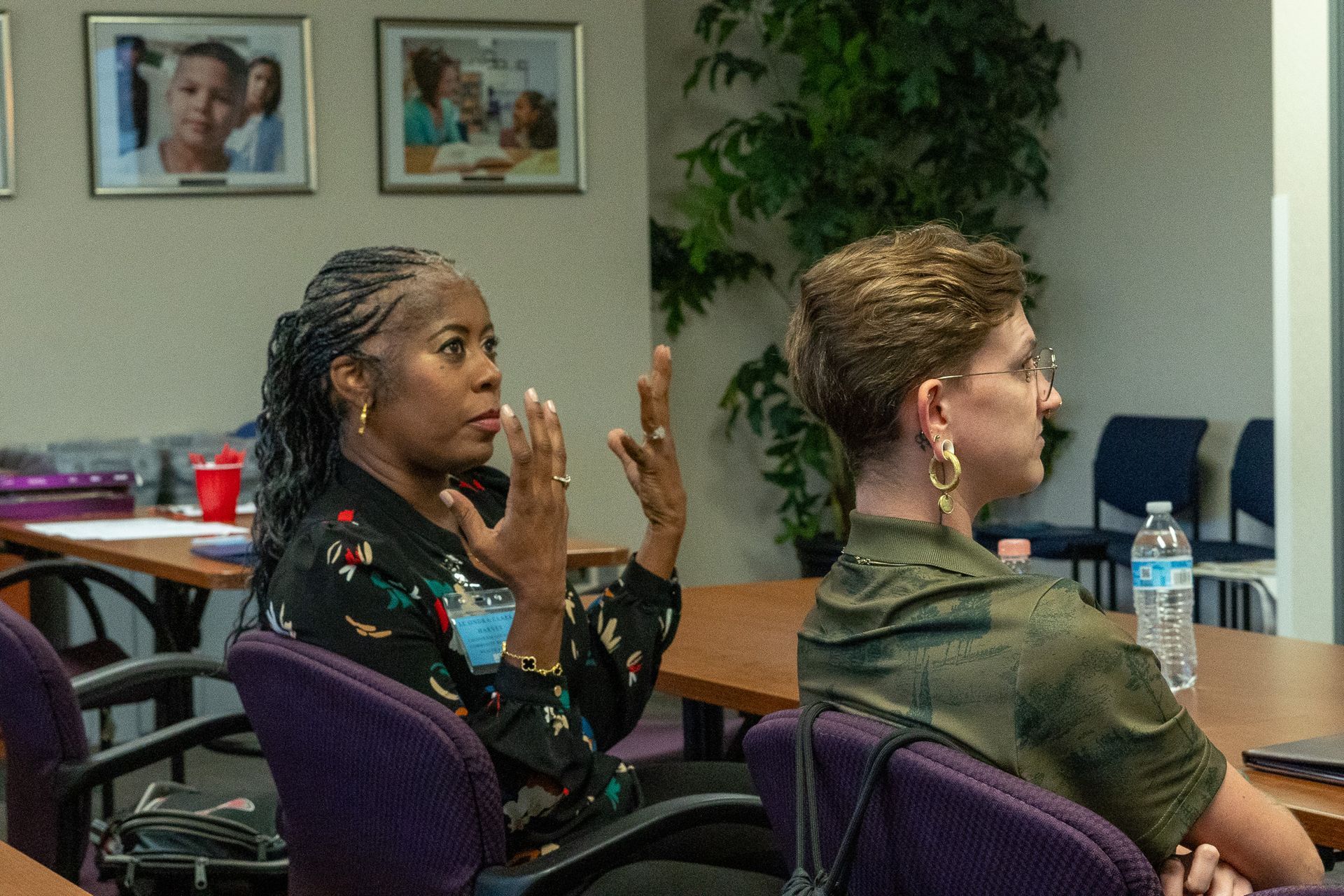 Two women seated in a meeting room, one speaking with raised hands while the other listens attentively.