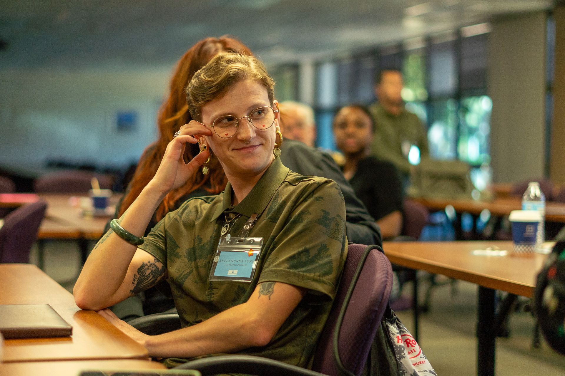 Smiling person in a camouflage shirt sitting at a table in a classroom or meeting room