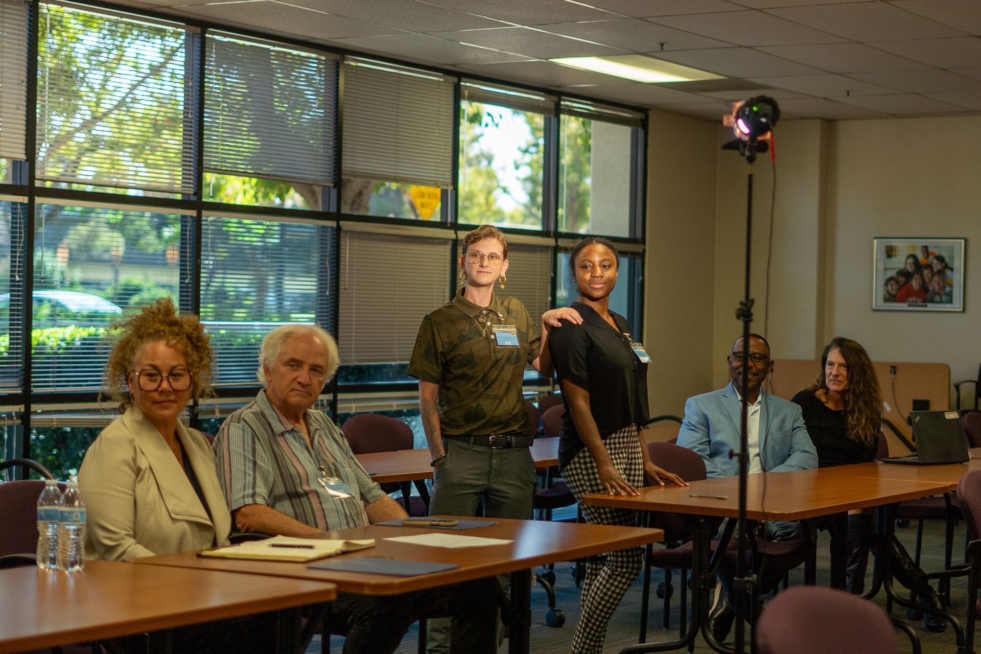 People seated at a conference table in a bright meeting room, with two standing near the back.