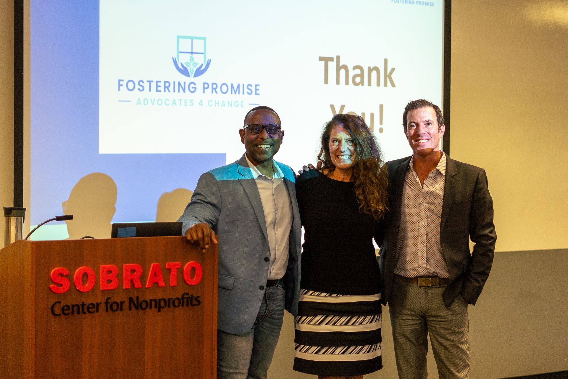 Three people posing at a Sobrato Center for Nonprofits event in front of a presentation screen.