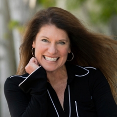 Smiling woman in black top outdoors, with wind blowing her hair