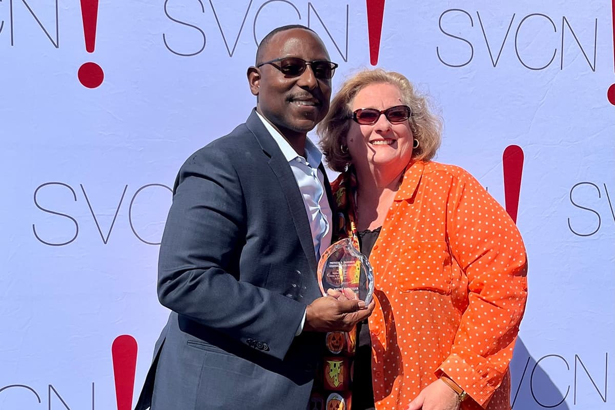 Two people posing with an award at an SVCN event, in front of a logo backdrop.