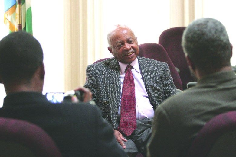Meeting discussion with a man in a suit speaking to two seated attendees in a room