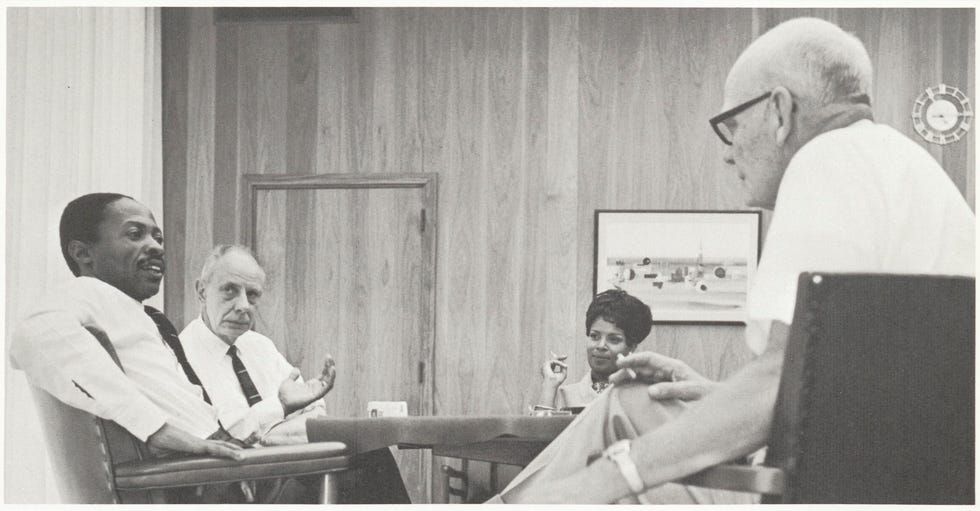 People seated around a conference table in a wood-paneled meeting room, discussing papers.