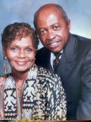 Smiling couple posed closely against a light blue background, wearing formal attire.