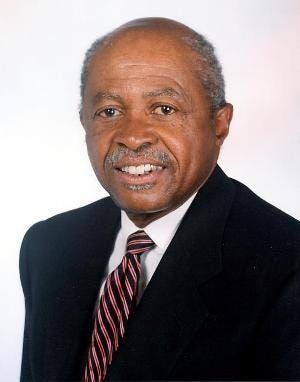 Portrait of a smiling man in a dark suit and striped tie against a light background