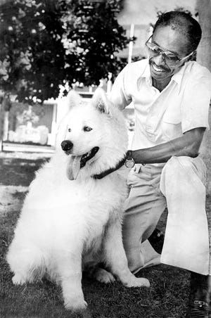 Man smiling beside a fluffy white dog outdoors, holding its collar.