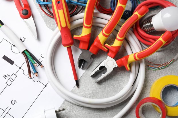 Utensili elettrici con manici rossi e gialli sopra uno schema elettrico e cavi su un banco da lavoro