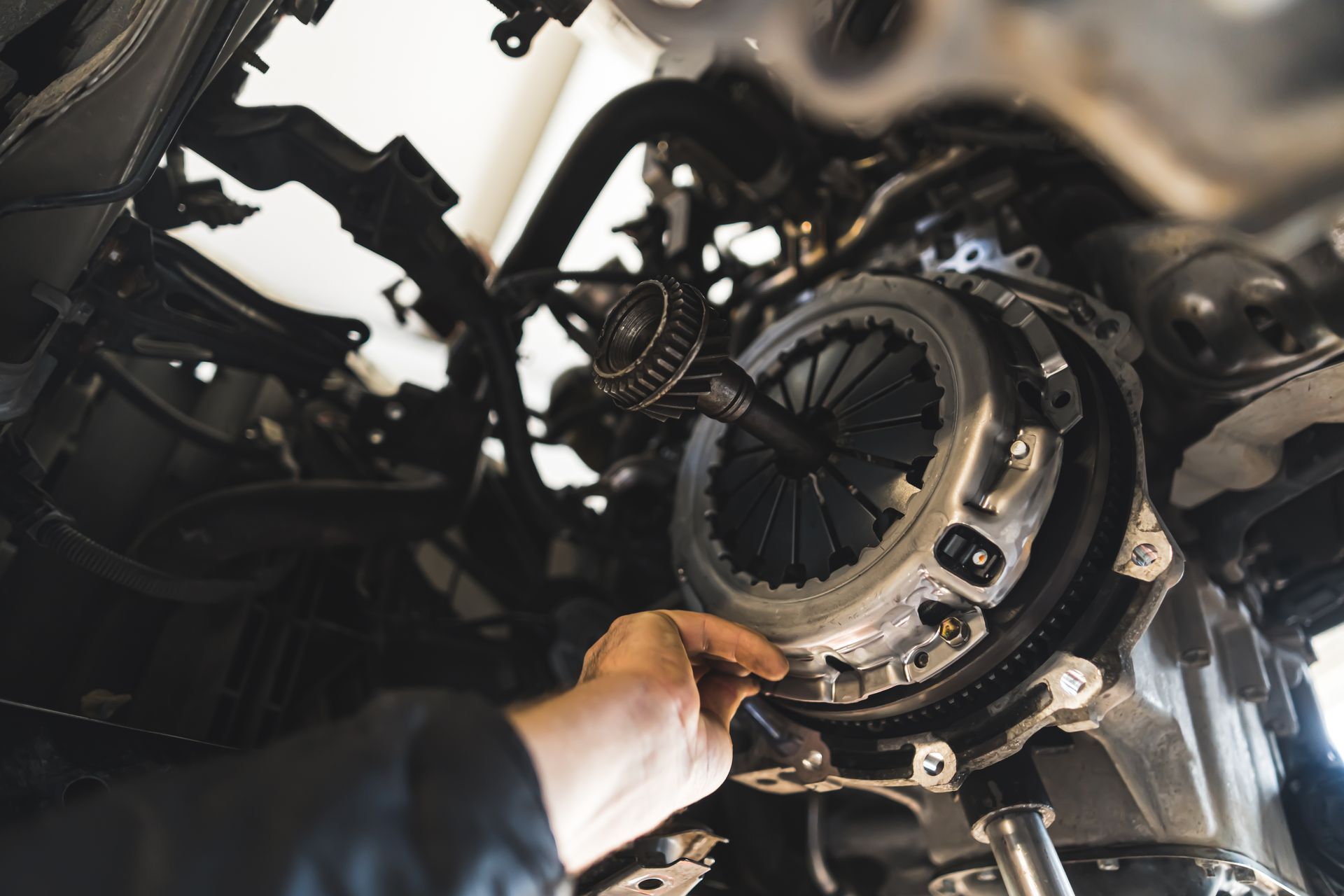 Person wearing gloves working on a car brake rotor and caliper in a garage.