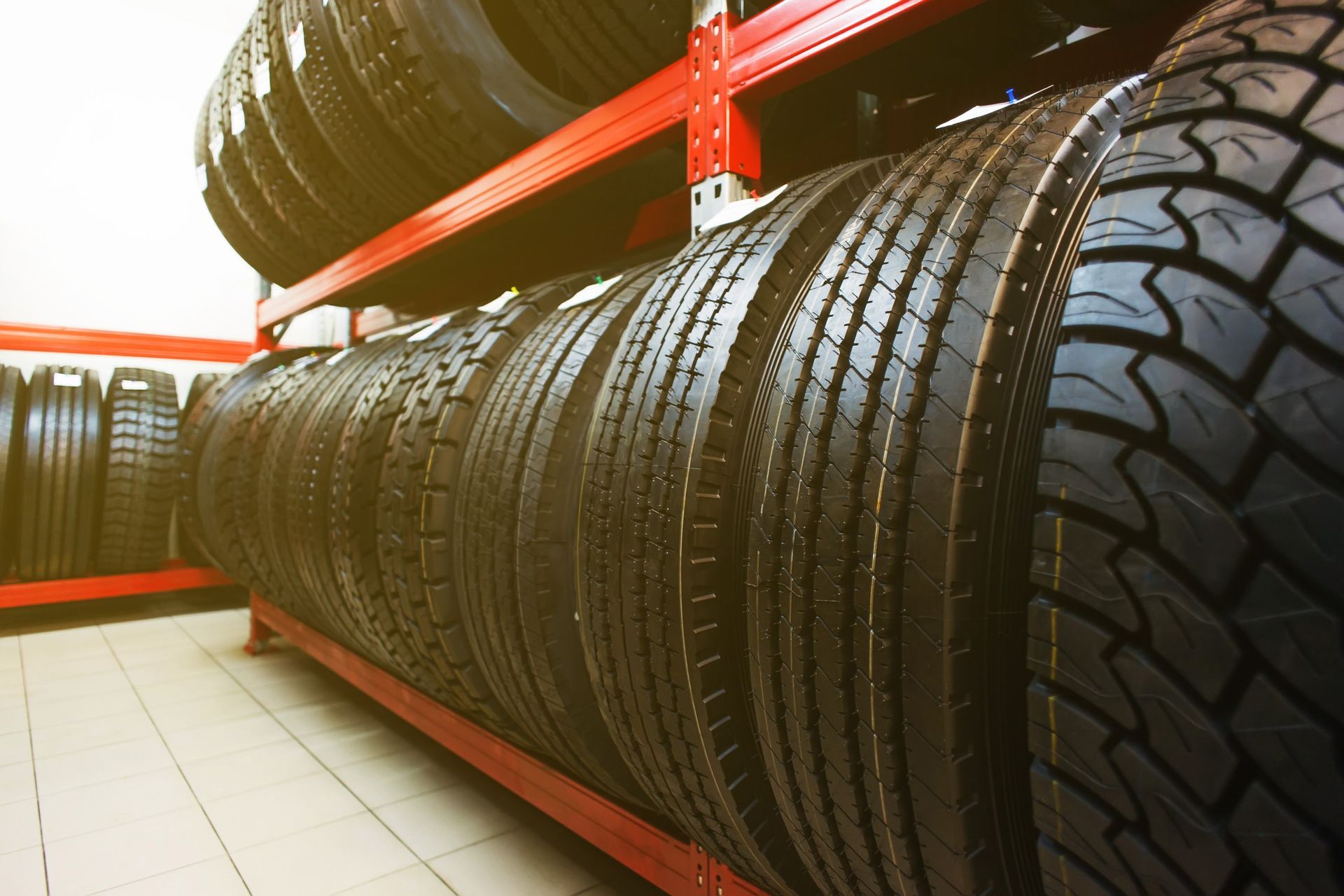 Tires stacked on red metal shelving in a store, viewed from a low angle.