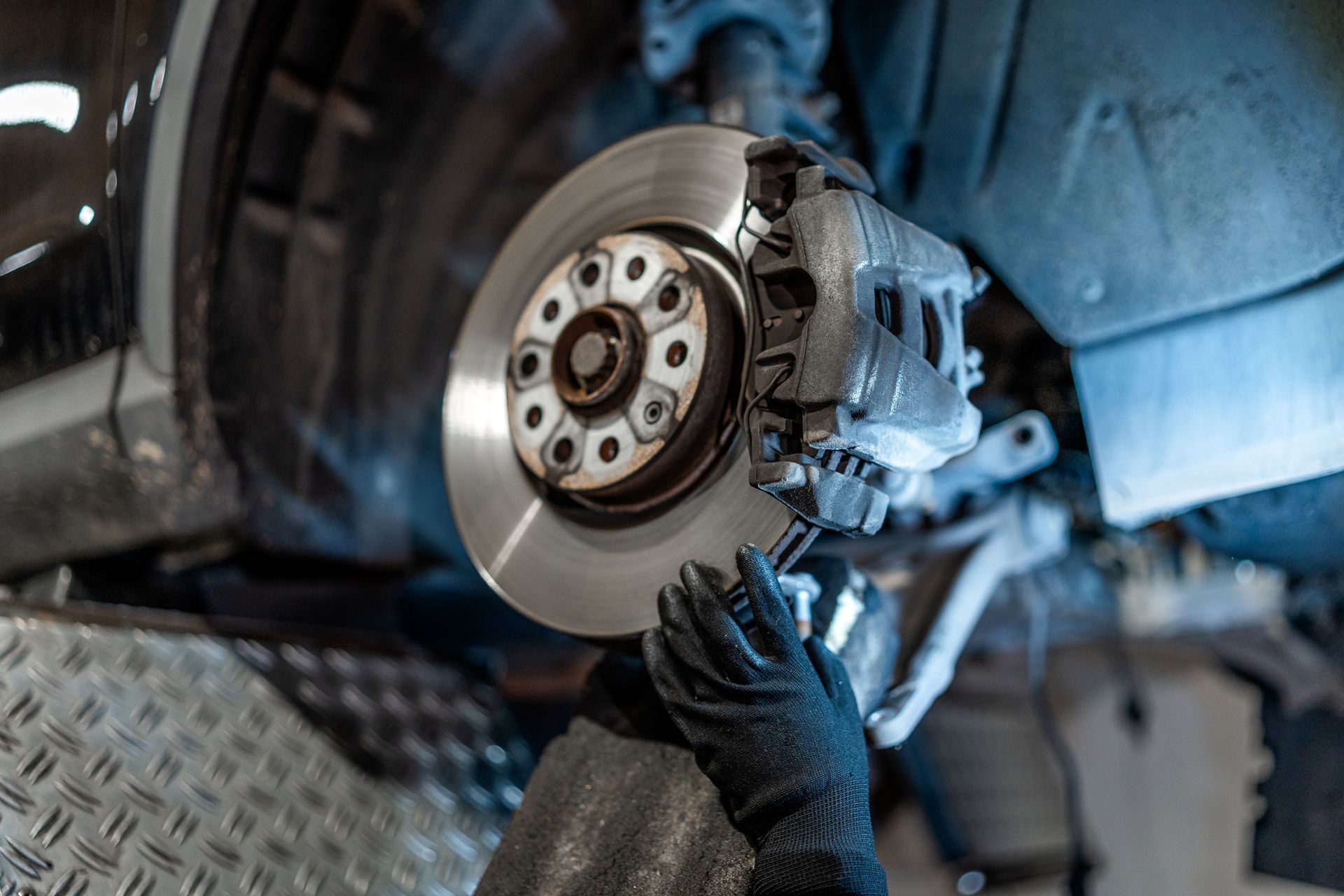 Person wearing gloves working on a car brake rotor and caliper in a garage.