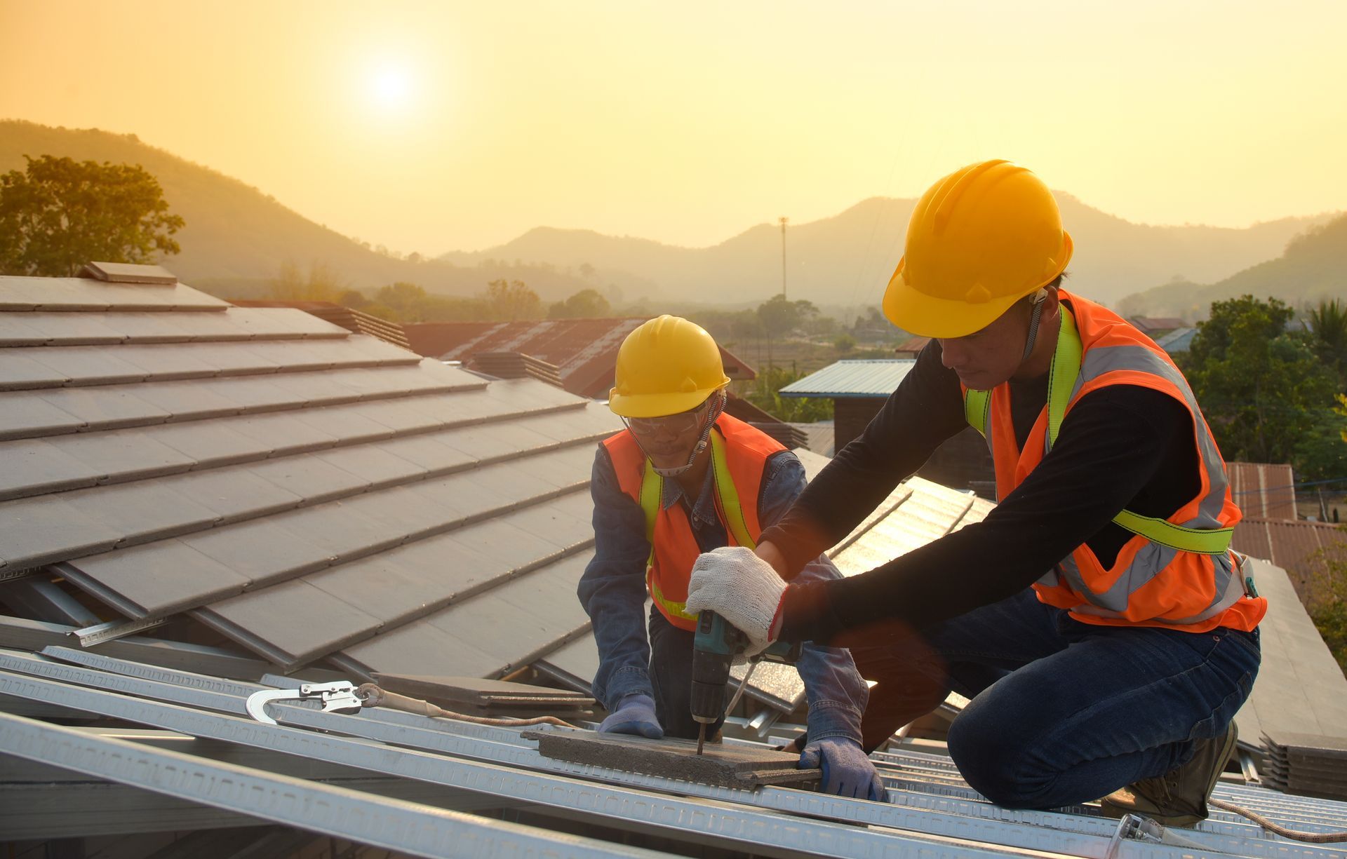 Two construction workers are working on a roof at sunset.