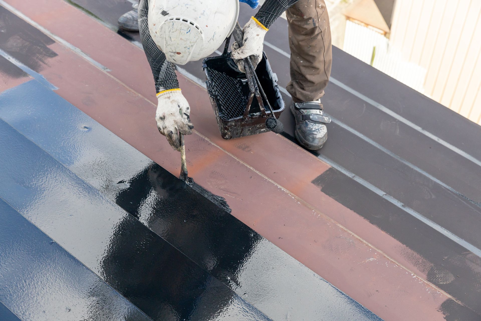 A man is painting a roof with black paint.