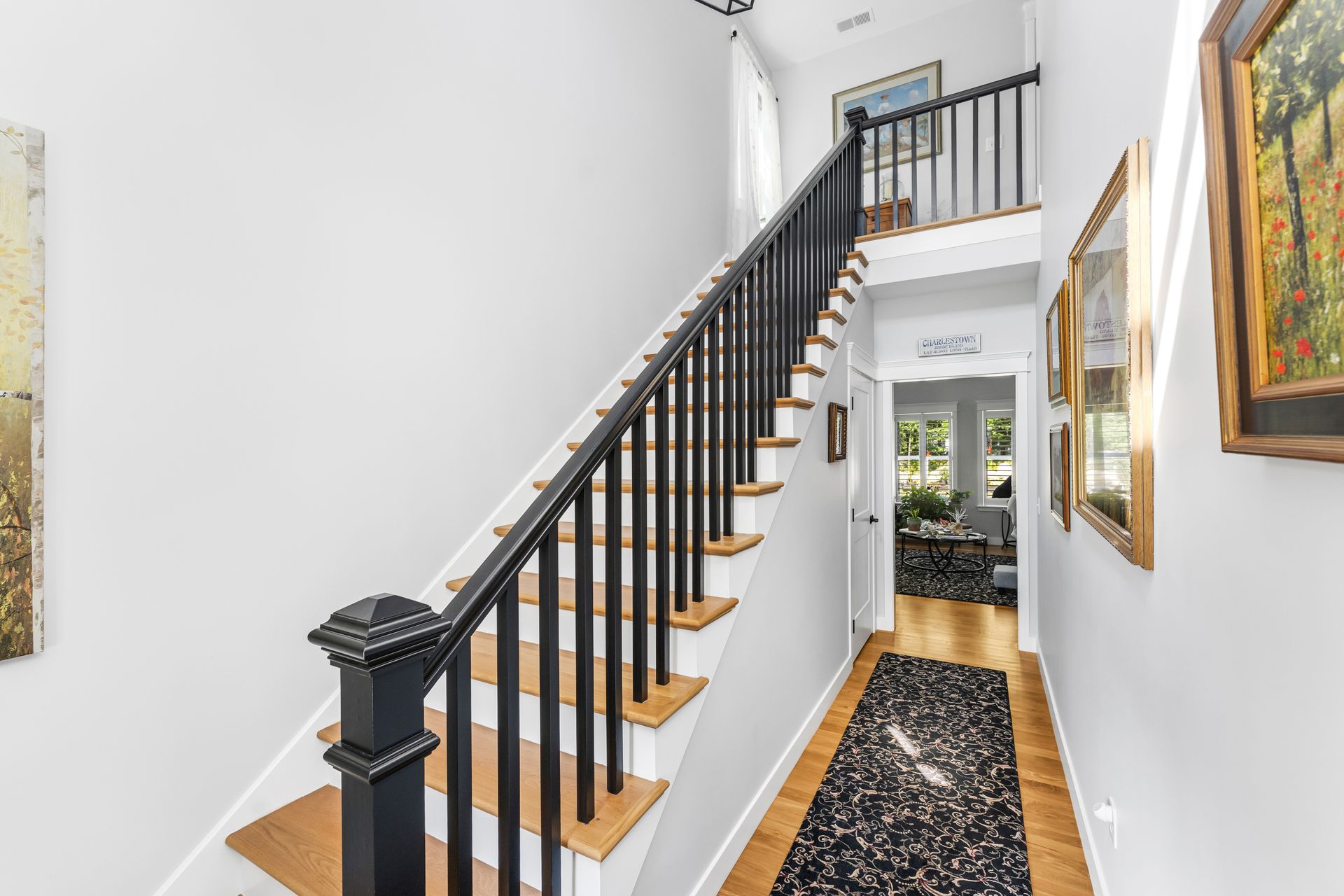 Bright hallway with a black-and-white staircase and framed artwork on white walls.