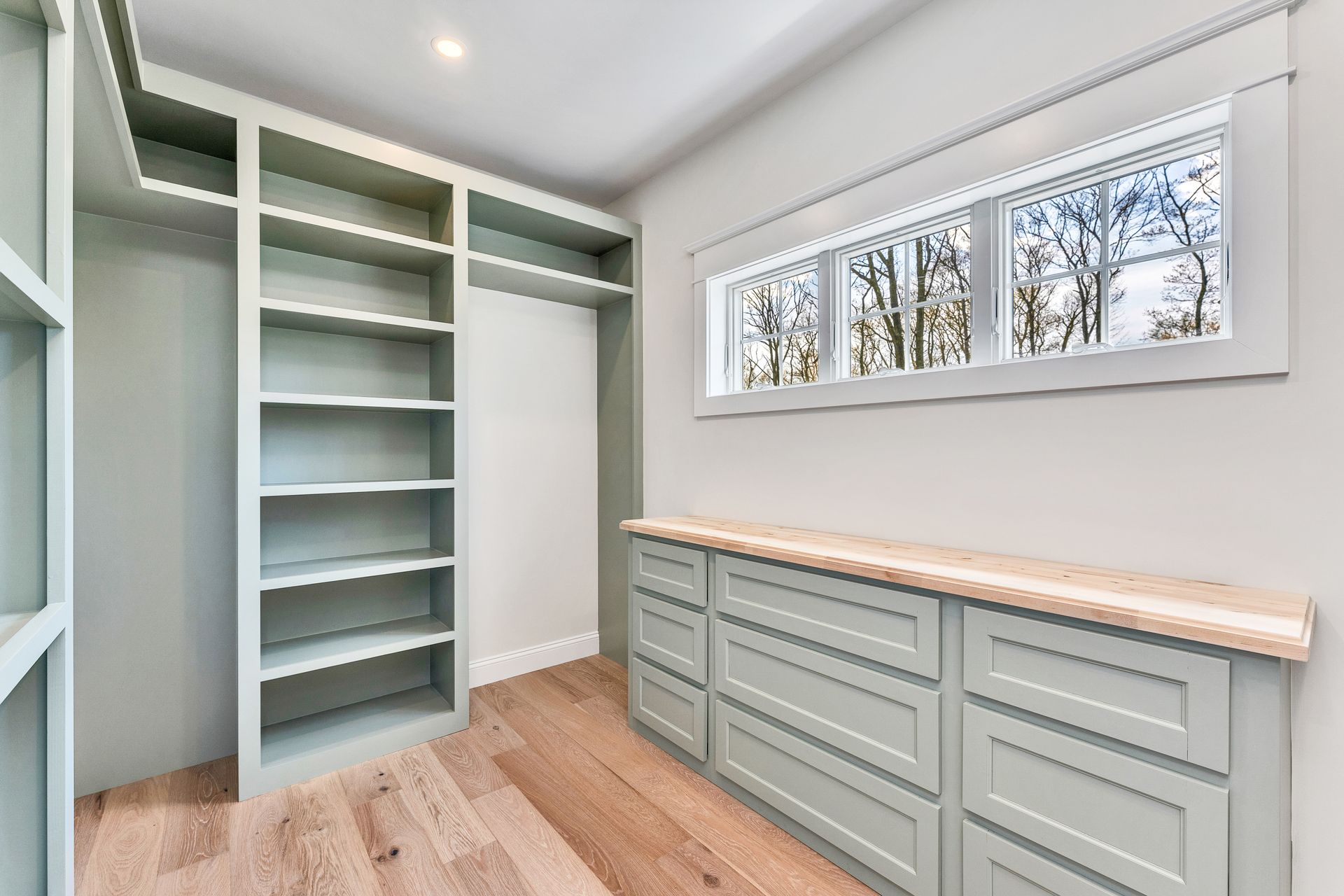 Bright closet with built-in shelves, drawers, and a wood countertop under narrow windows