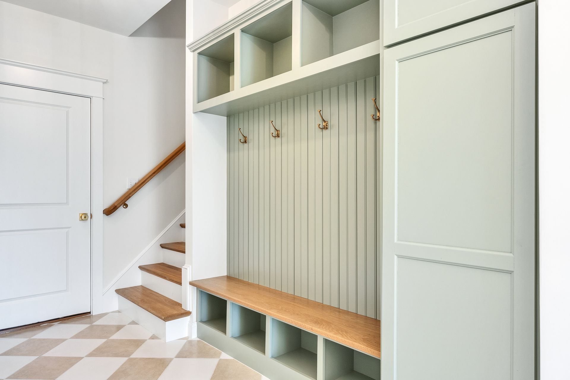 Built-in mudroom bench and cubbies in a light green entryway beside a staircase
