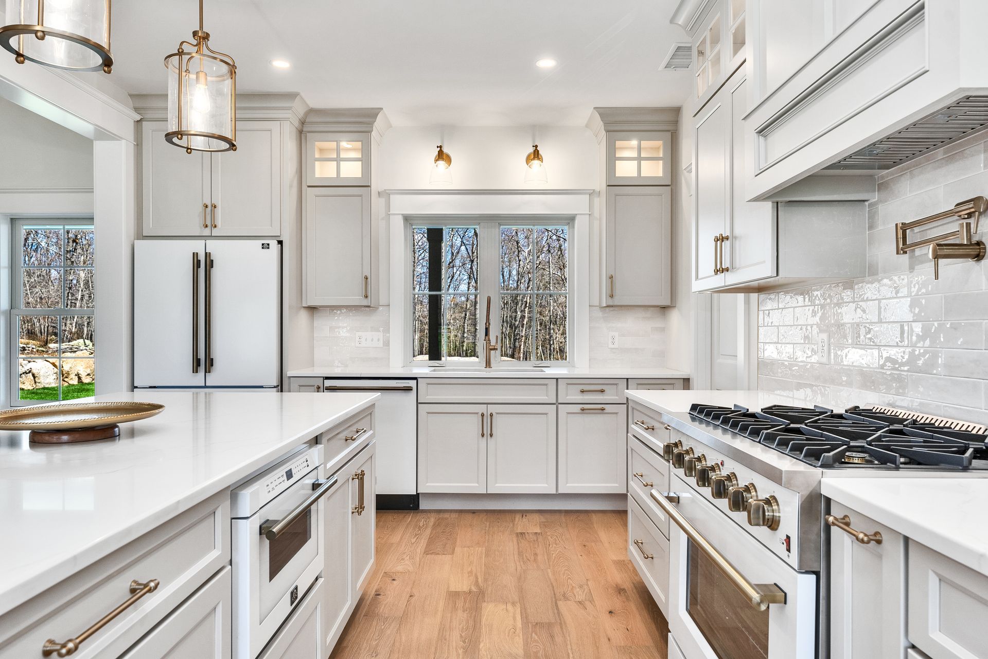 Bright white modern kitchen with stainless steel appliances, wooden floors, and large windows