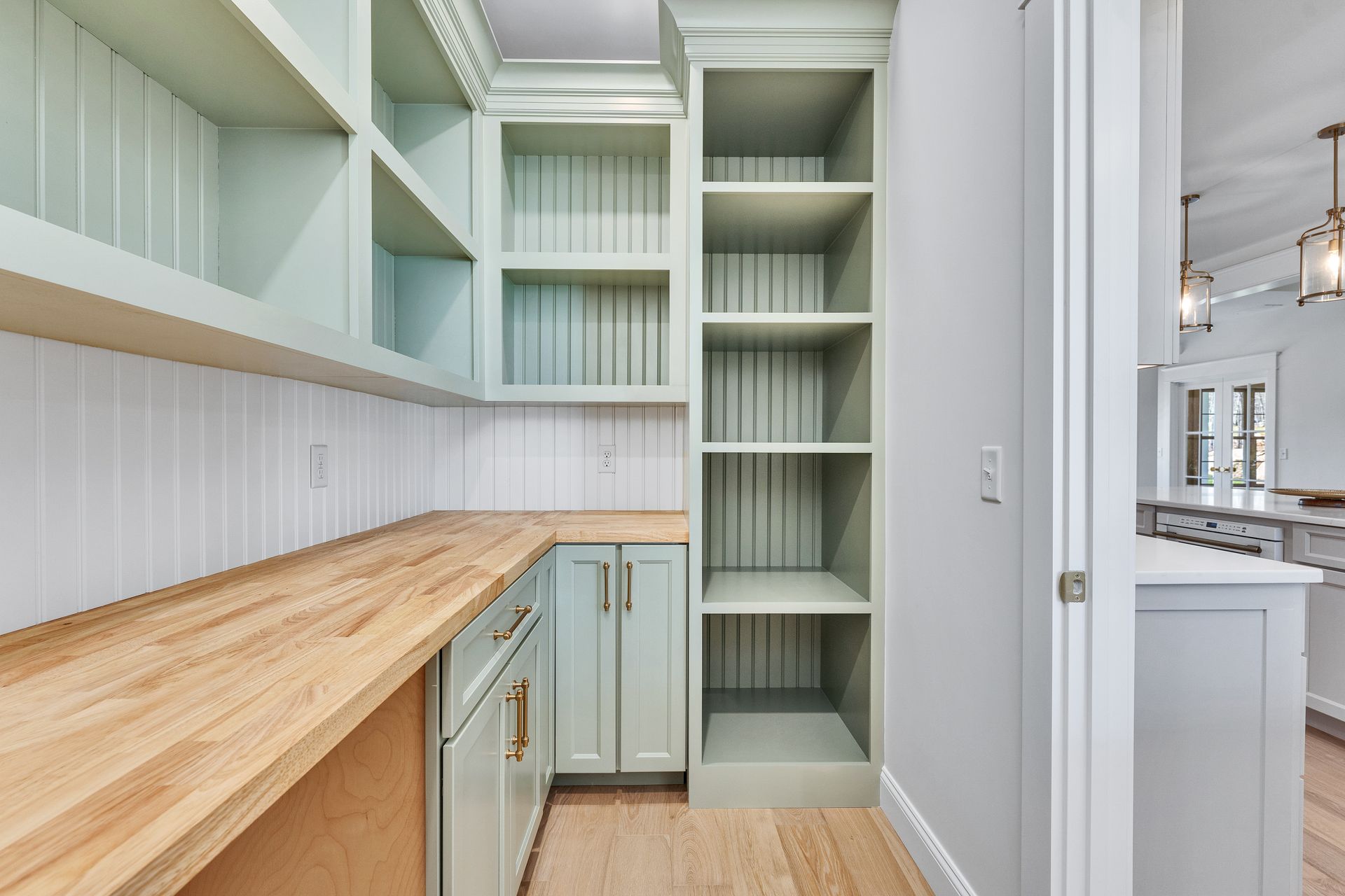 Built-in pantry with pale green cabinets, wooden countertop, and open shelving in a bright kitchen nook