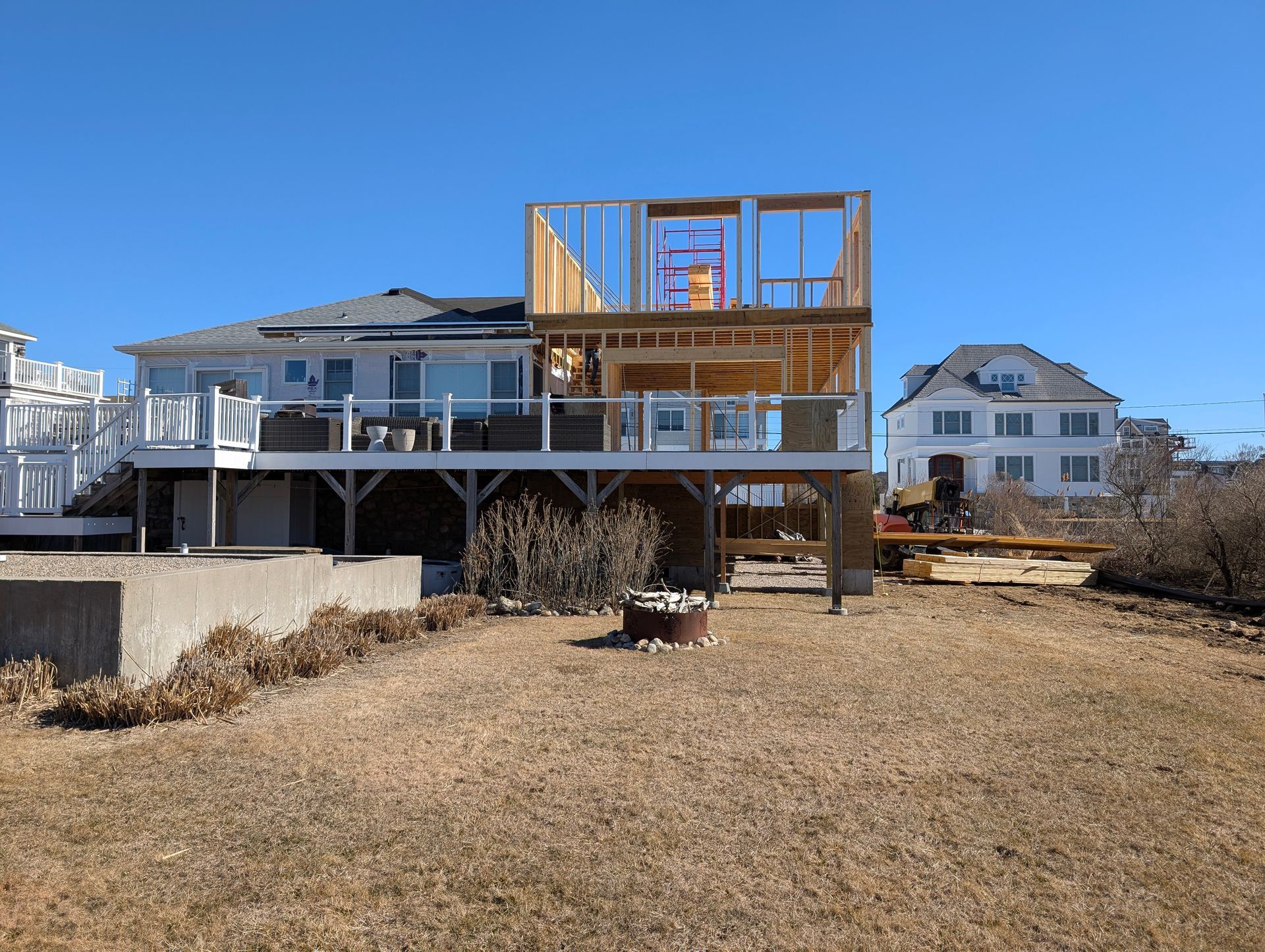 House under construction with exposed wooden framing beside a finished white home on a dry lot.