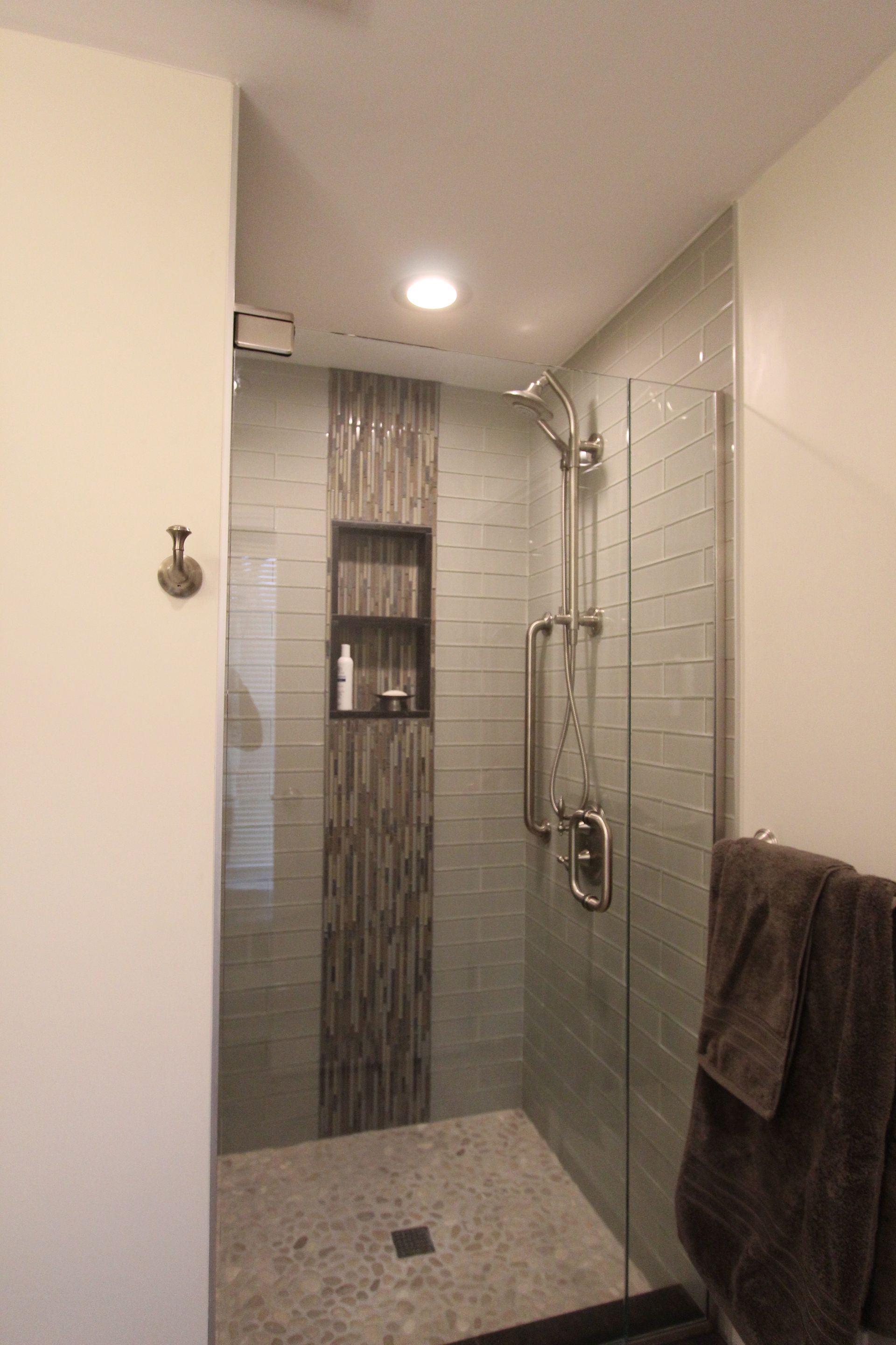 Shower with glass doors, light gray tile walls, and a dark tile accent strip with a built-in shelf.
