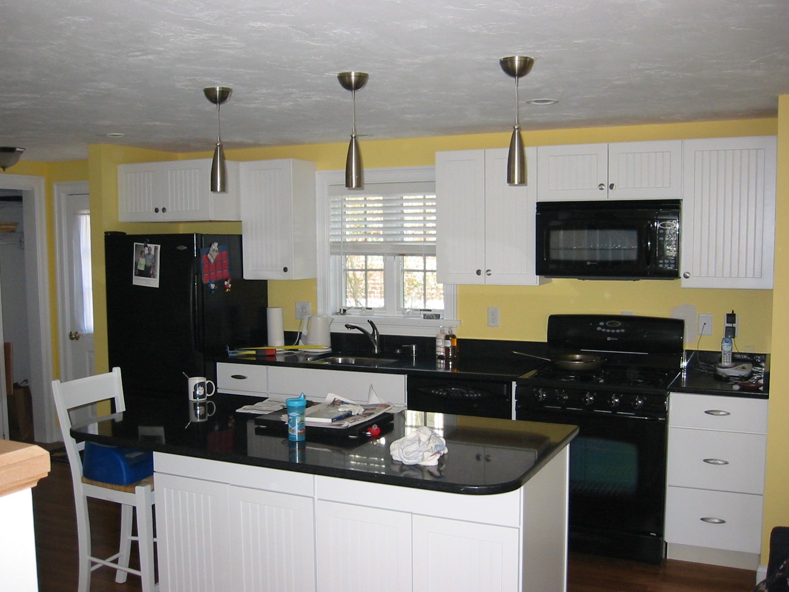 Kitchen with white cabinets, black appliances, yellow walls, and a black countertop island.