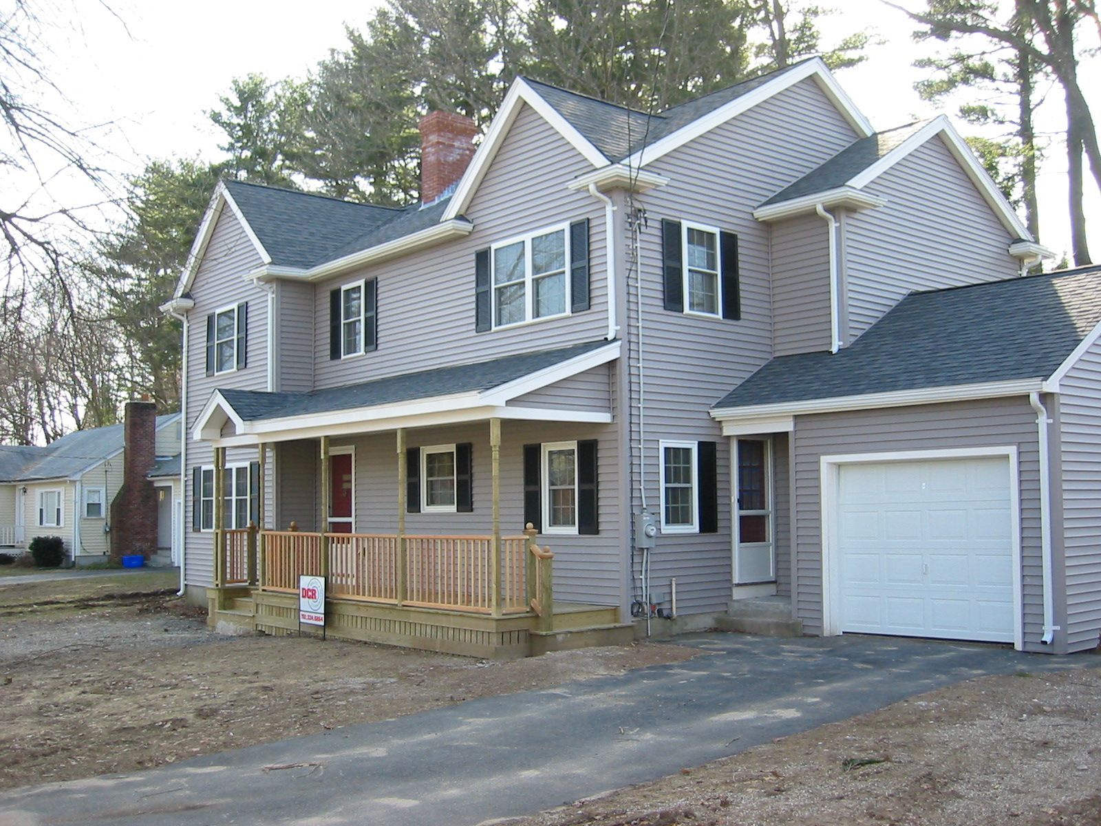 Two-story house with gray siding, black shutters, porch, and a garage. Driveway in front.