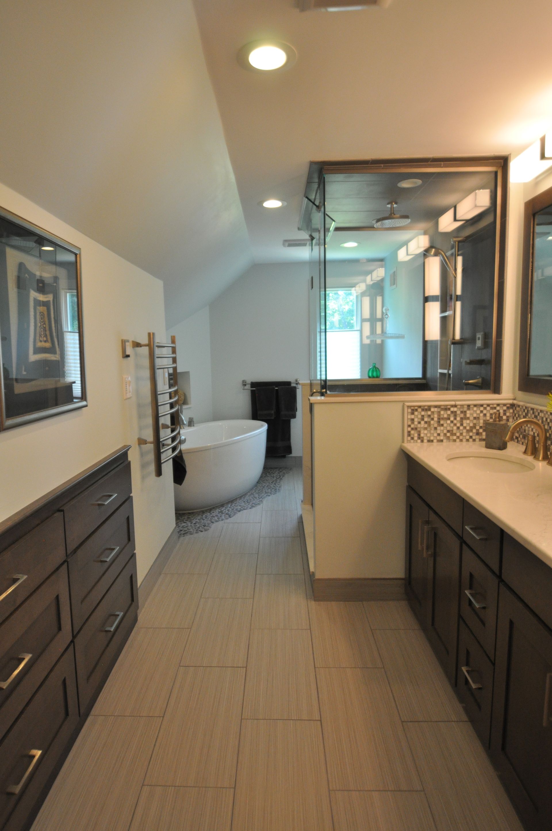 Long, narrow bathroom with a tub, vanity, and cabinets; light beige walls and floors.