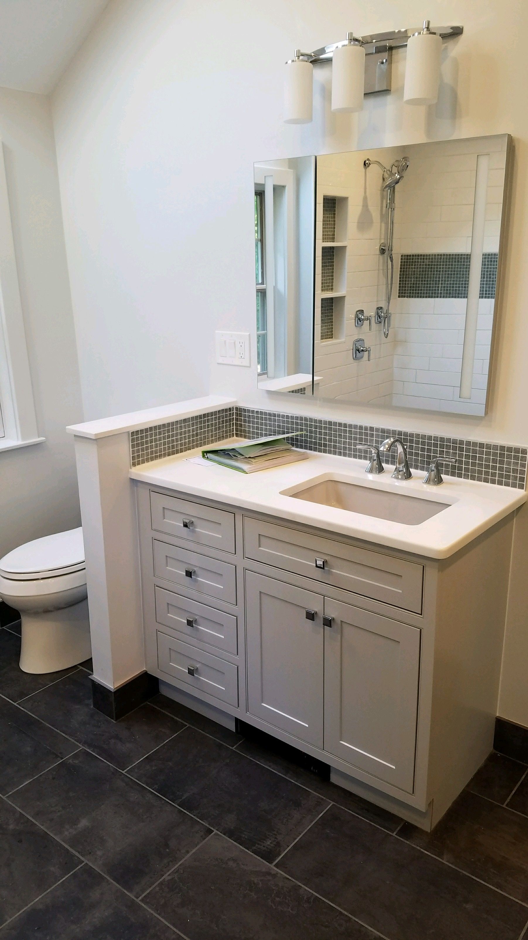 Bathroom with gray vanity, sink, mirror, and tile accent. Dark floor and white walls.