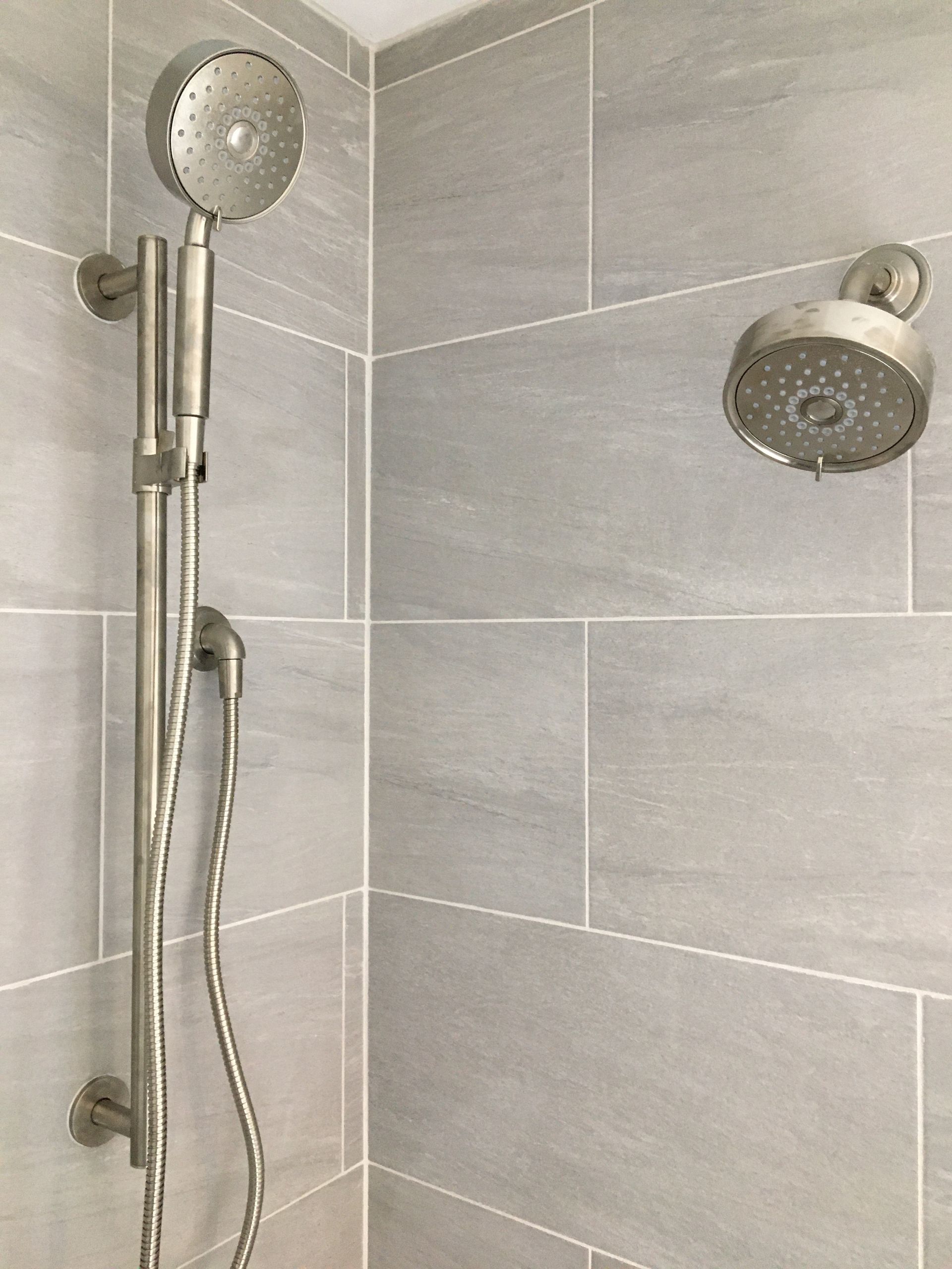 Silver shower fixtures on gray tiled wall.