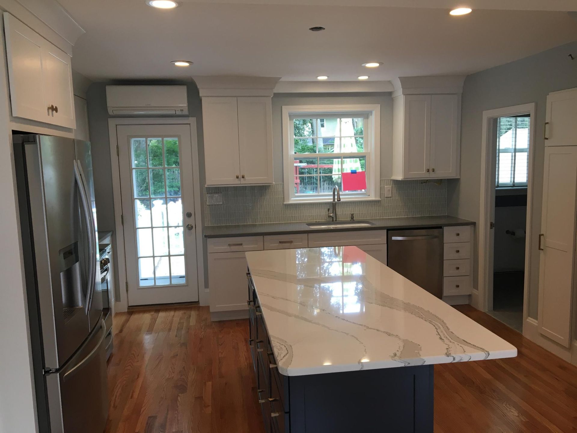 Modern kitchen with white cabinets, stainless steel appliances, and a dark blue island with a white countertop.