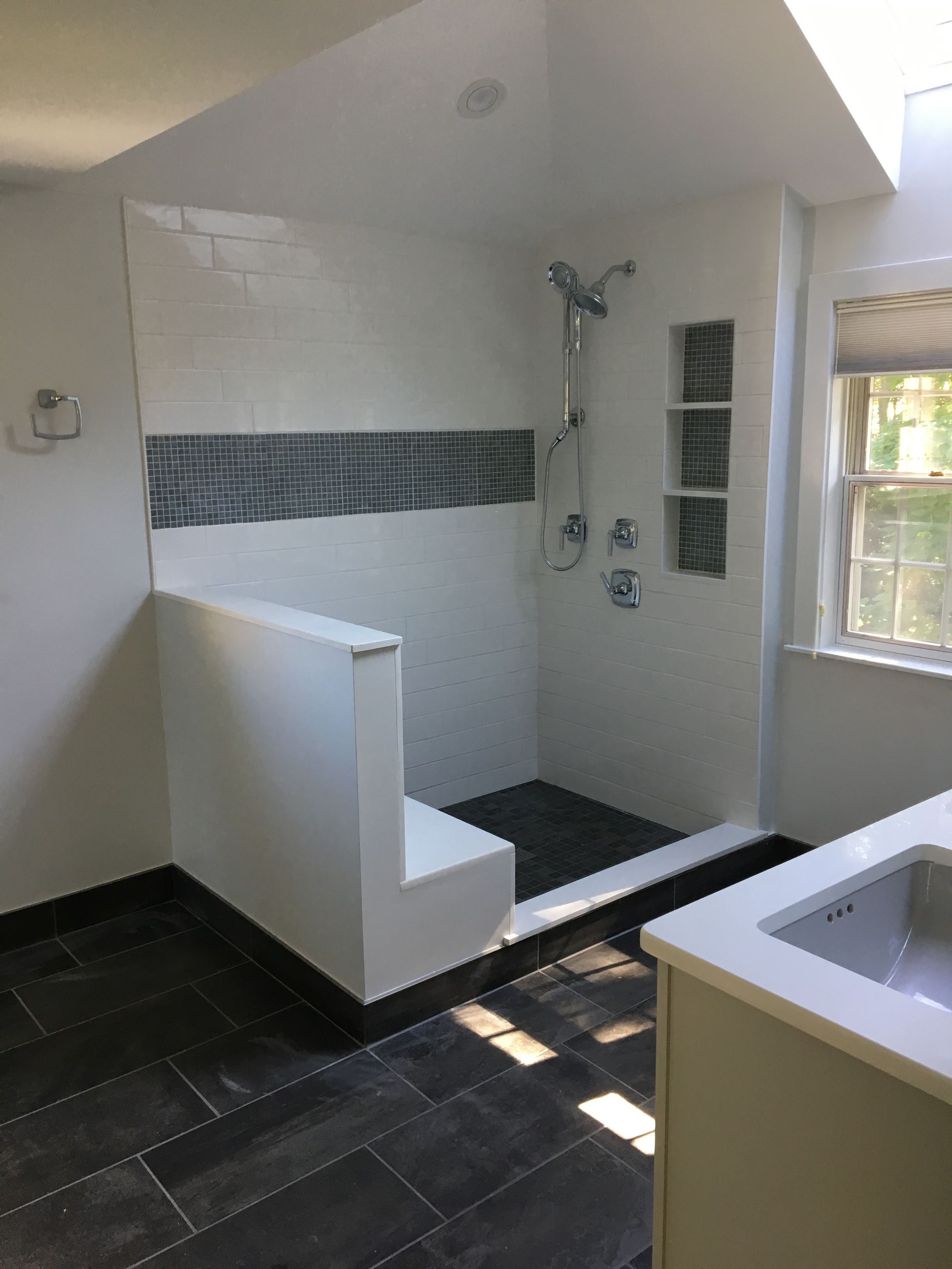 Modern bathroom with a walk-in shower, dark tile floor, white walls, and glass block window.