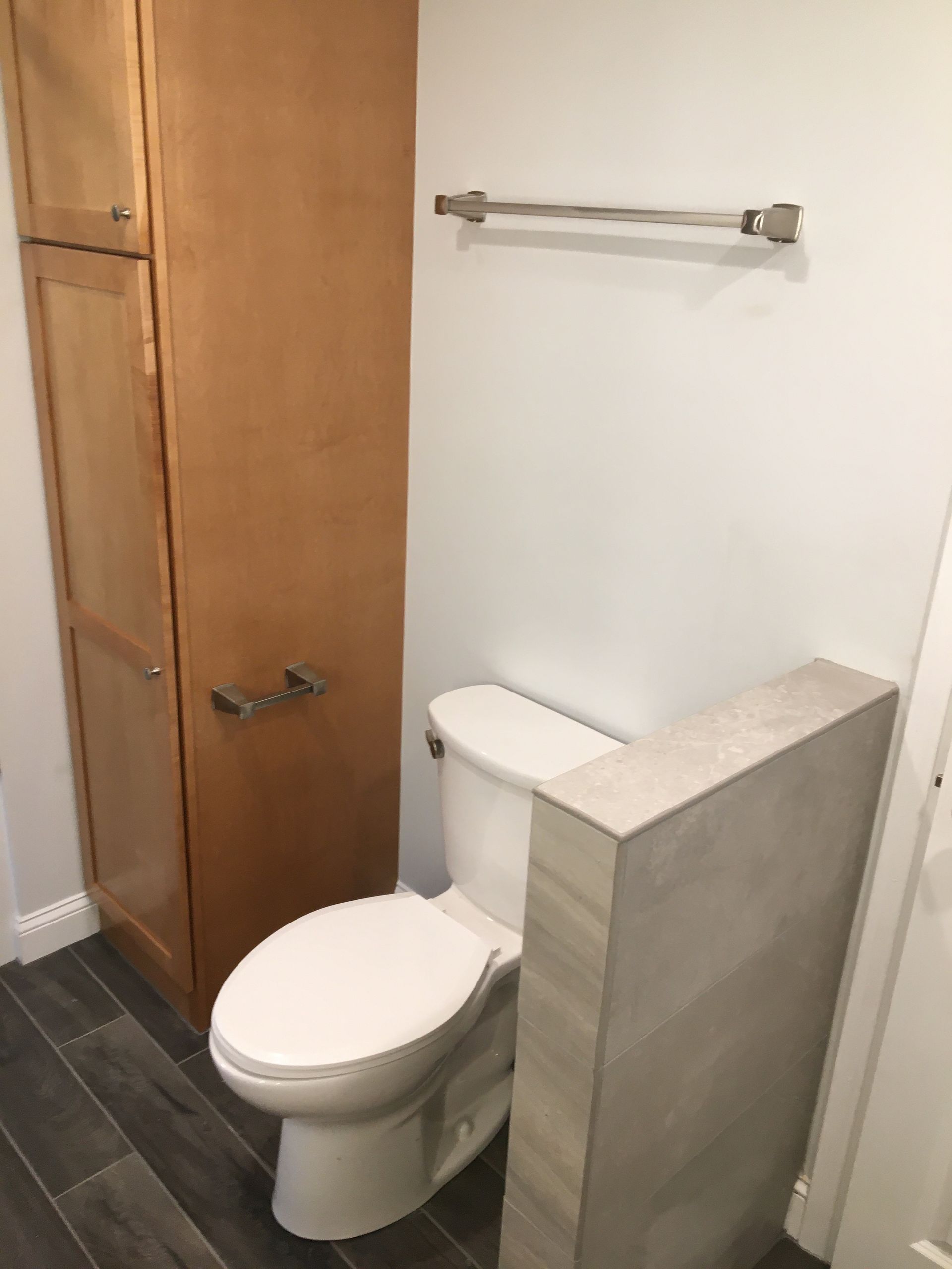 Bathroom with a toilet, tall cabinet, towel rack, and gray tile floor.