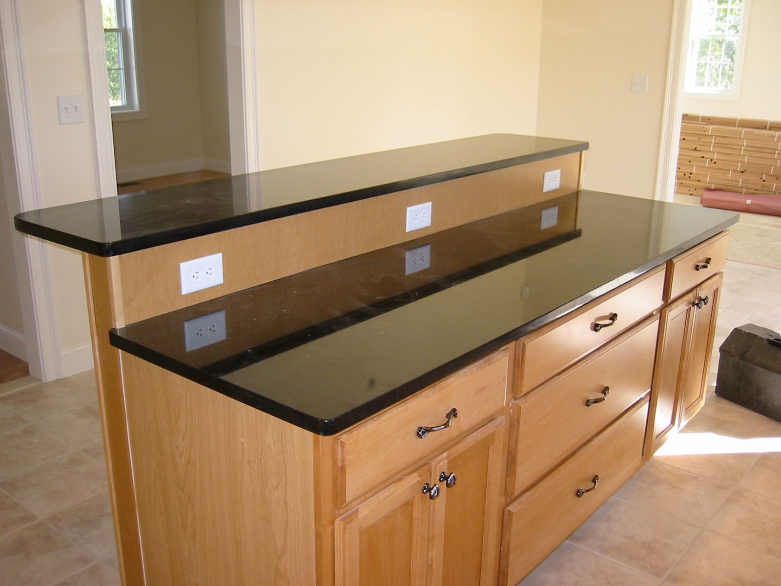 Kitchen island with black granite countertops and light wood cabinets, built-in outlets.