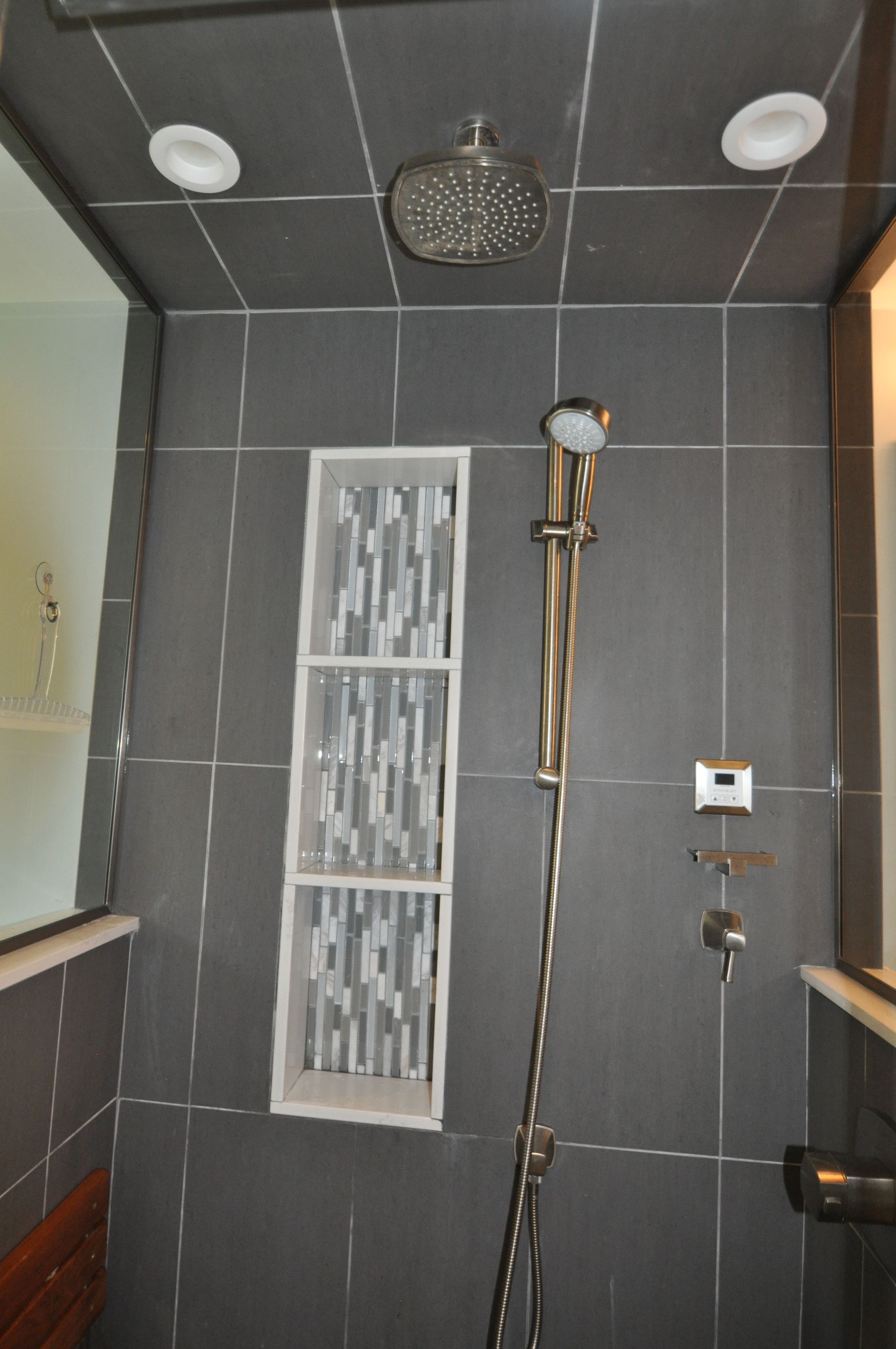 Gray-tiled shower with a mosaic-tiled shelf and chrome showerhead, faucet, and handheld wand.