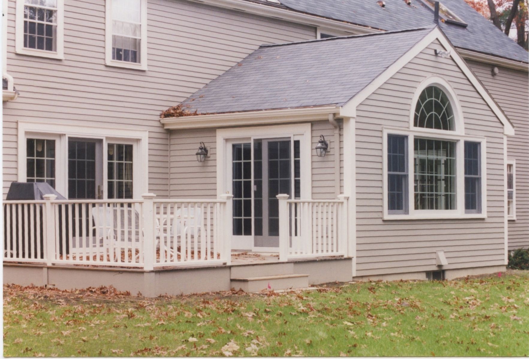 Back of a house with a deck and an addition. Light gray siding, white railings, and a gray roof.