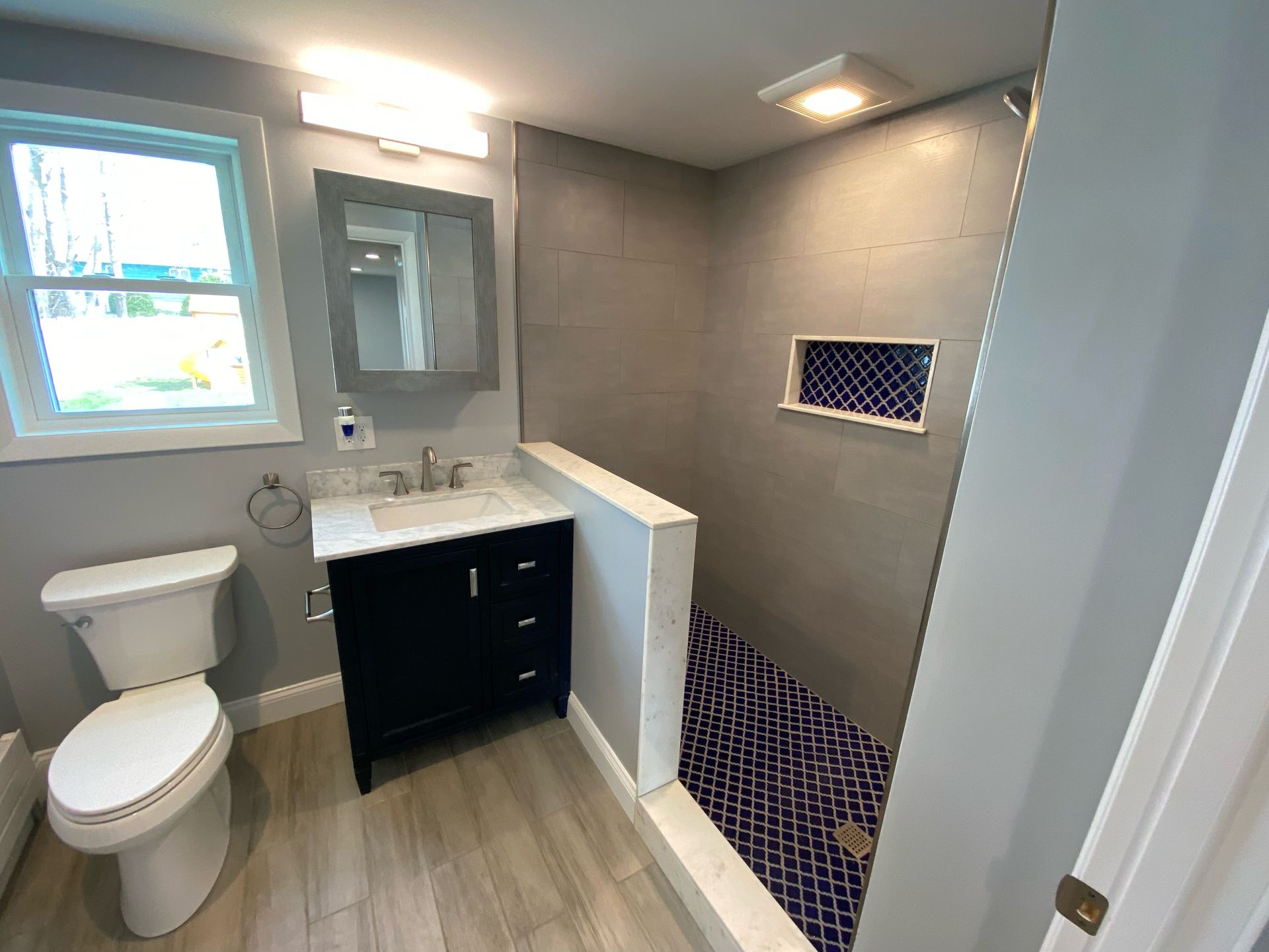 Bathroom with gray walls, dark blue vanity, and walk-in shower with blue mosaic floor.