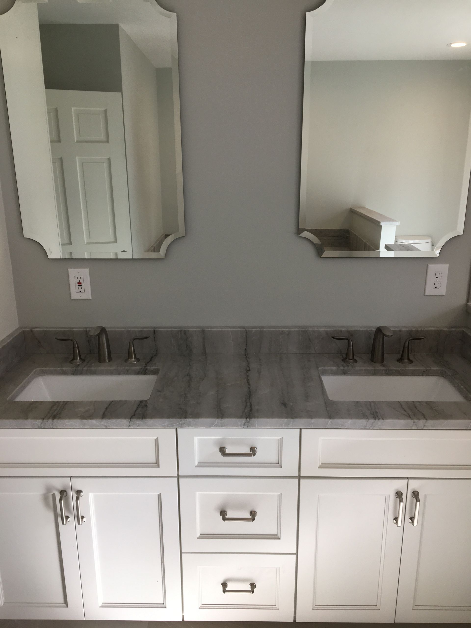 Bathroom with white cabinets, gray countertop, two sinks, and ornate mirrors.
