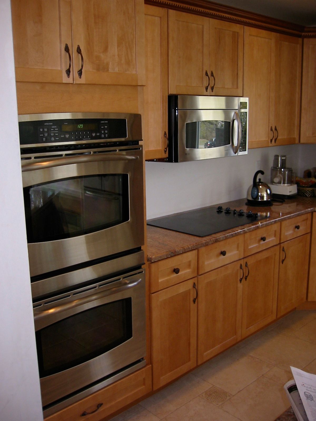 Kitchen with light wood cabinets, stainless steel double oven, microwave, and stovetop.