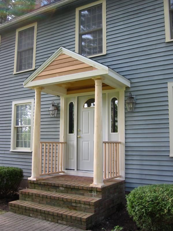 Blue house with a white door, covered by a wooden portico with light-colored pillars and a brick stair.