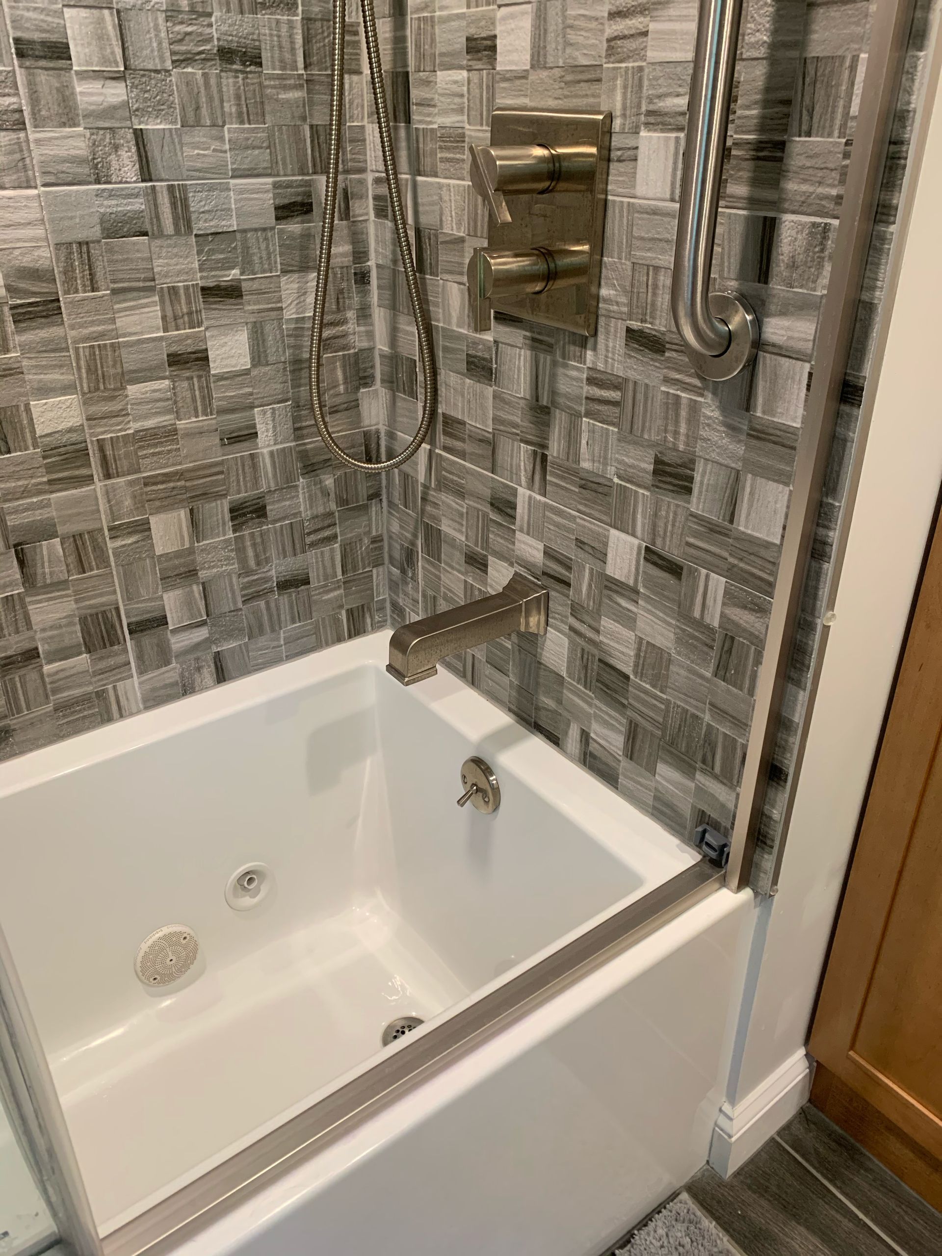 White bathtub with gray tile surround, showerhead and fixtures.