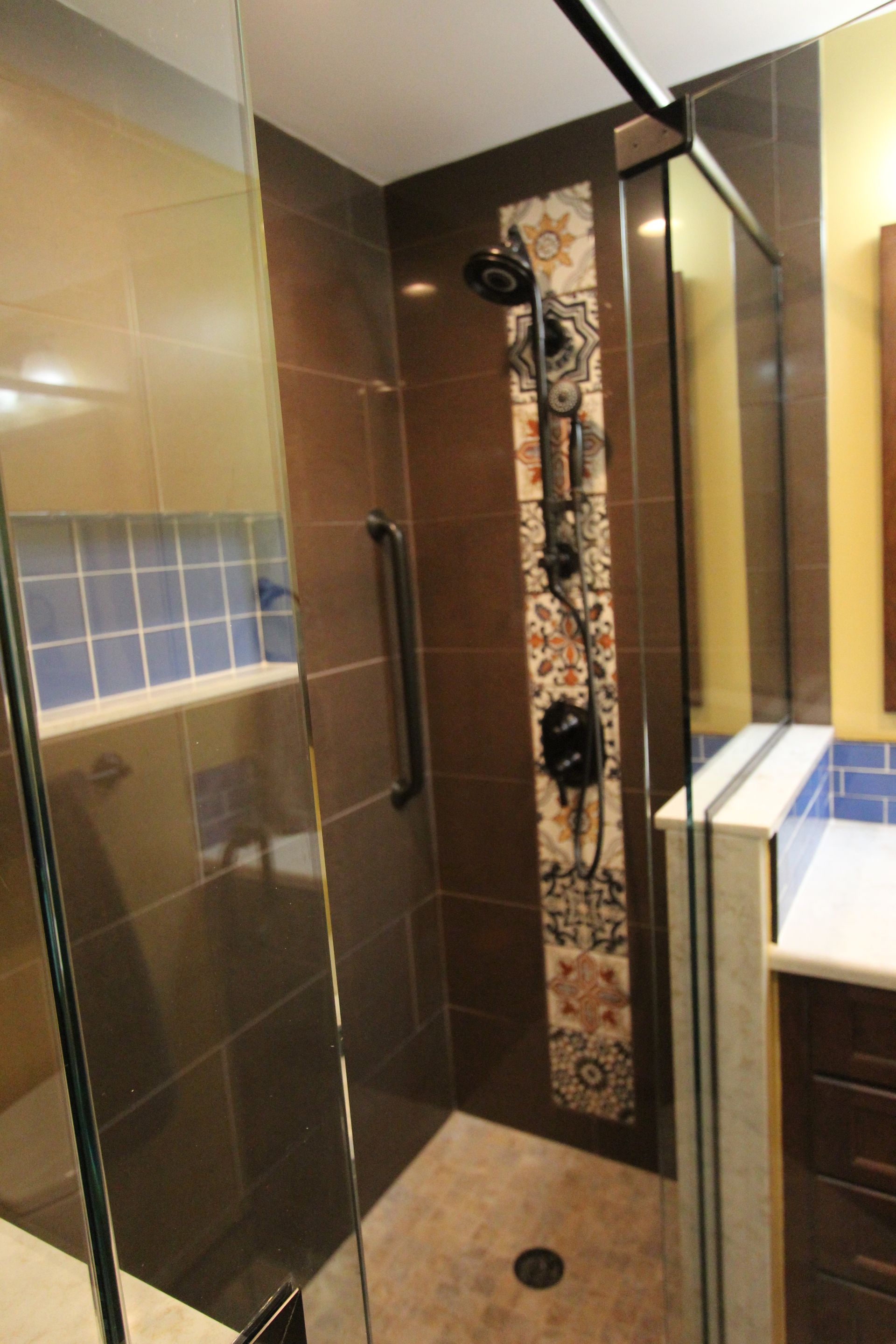Bathroom with brown tile shower, glass door, and decorative tile strip. Grab bar present.