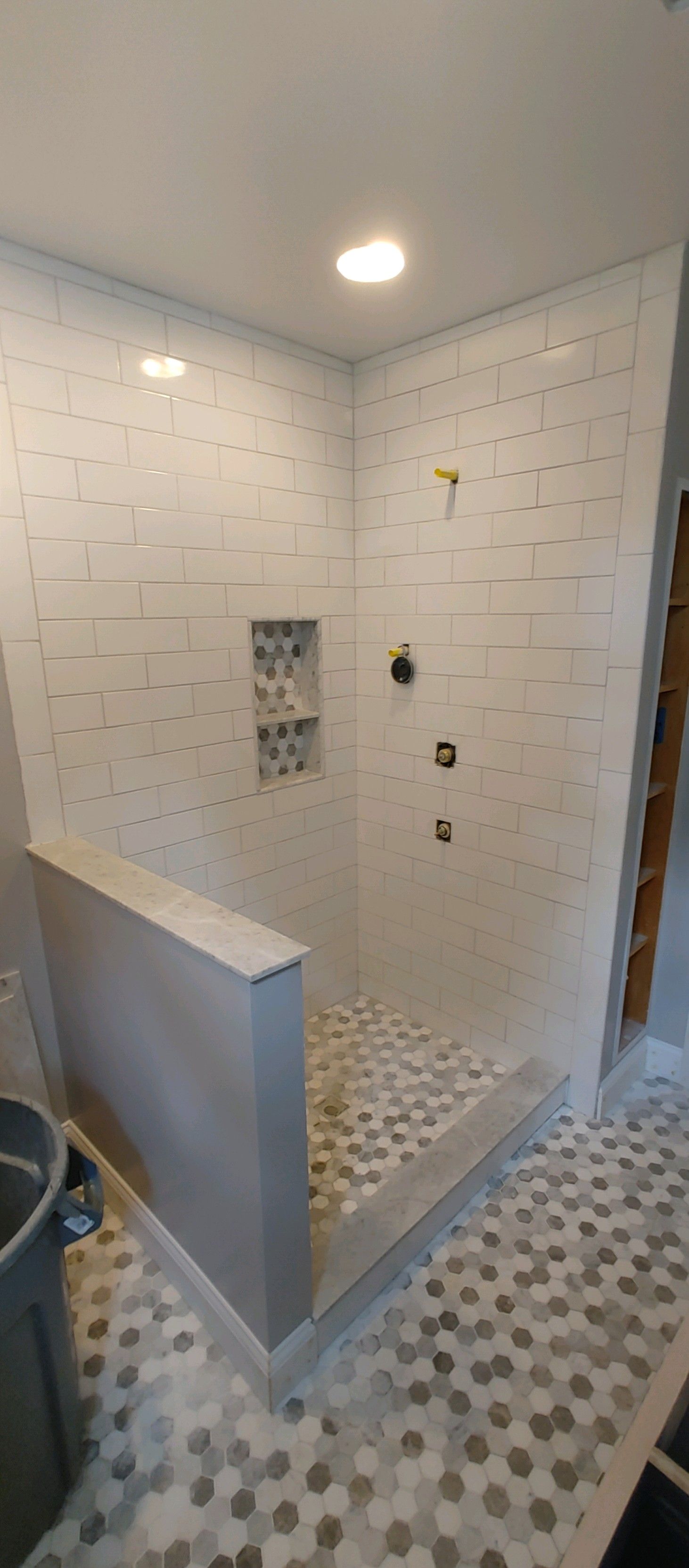 A newly tiled shower with pebble floor, gray curb, and hexagon tile floor.