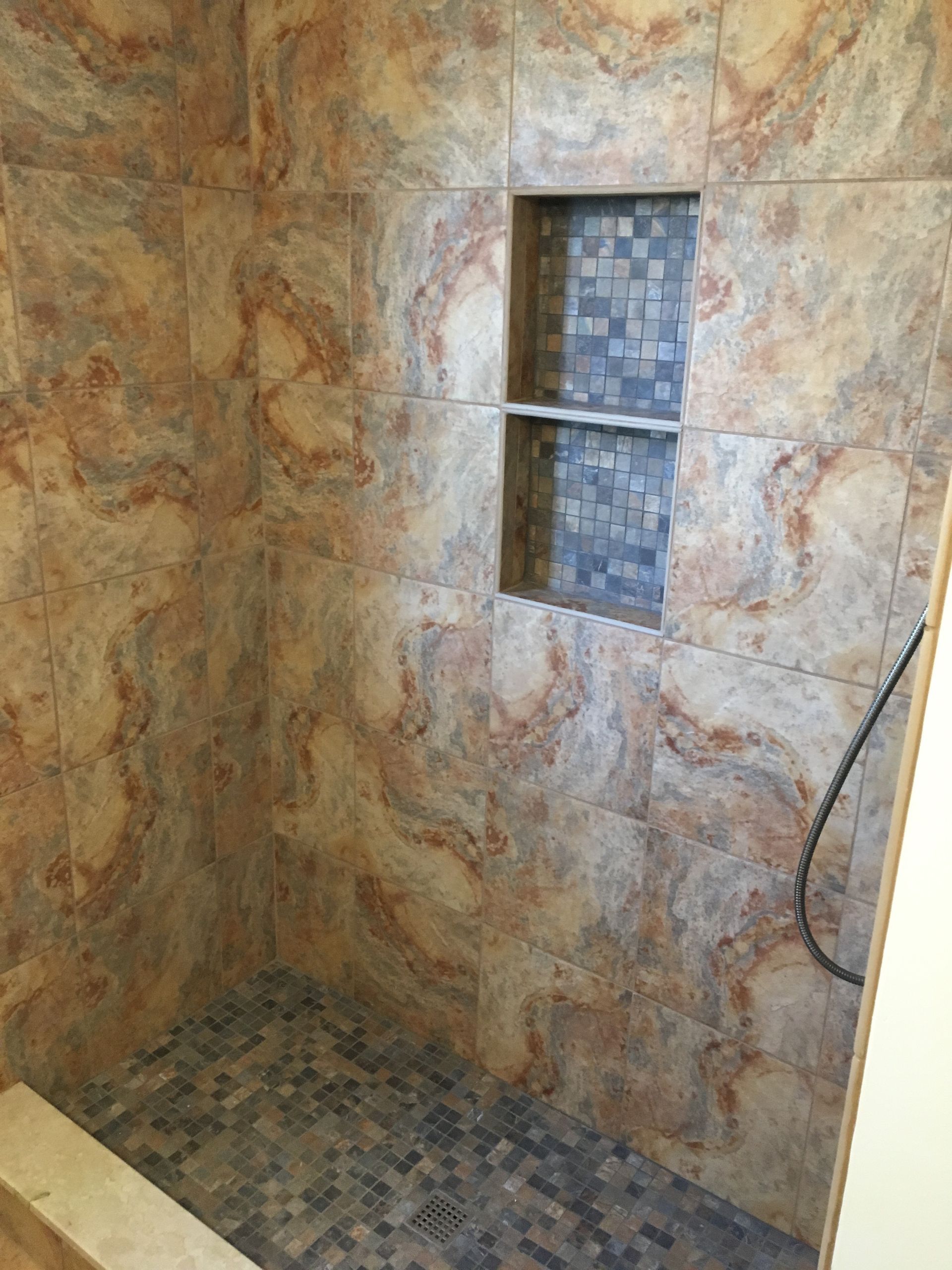 Bathroom shower with multi-colored marbled tile walls, small mosaic tile accent in the niche, and pebble floor.