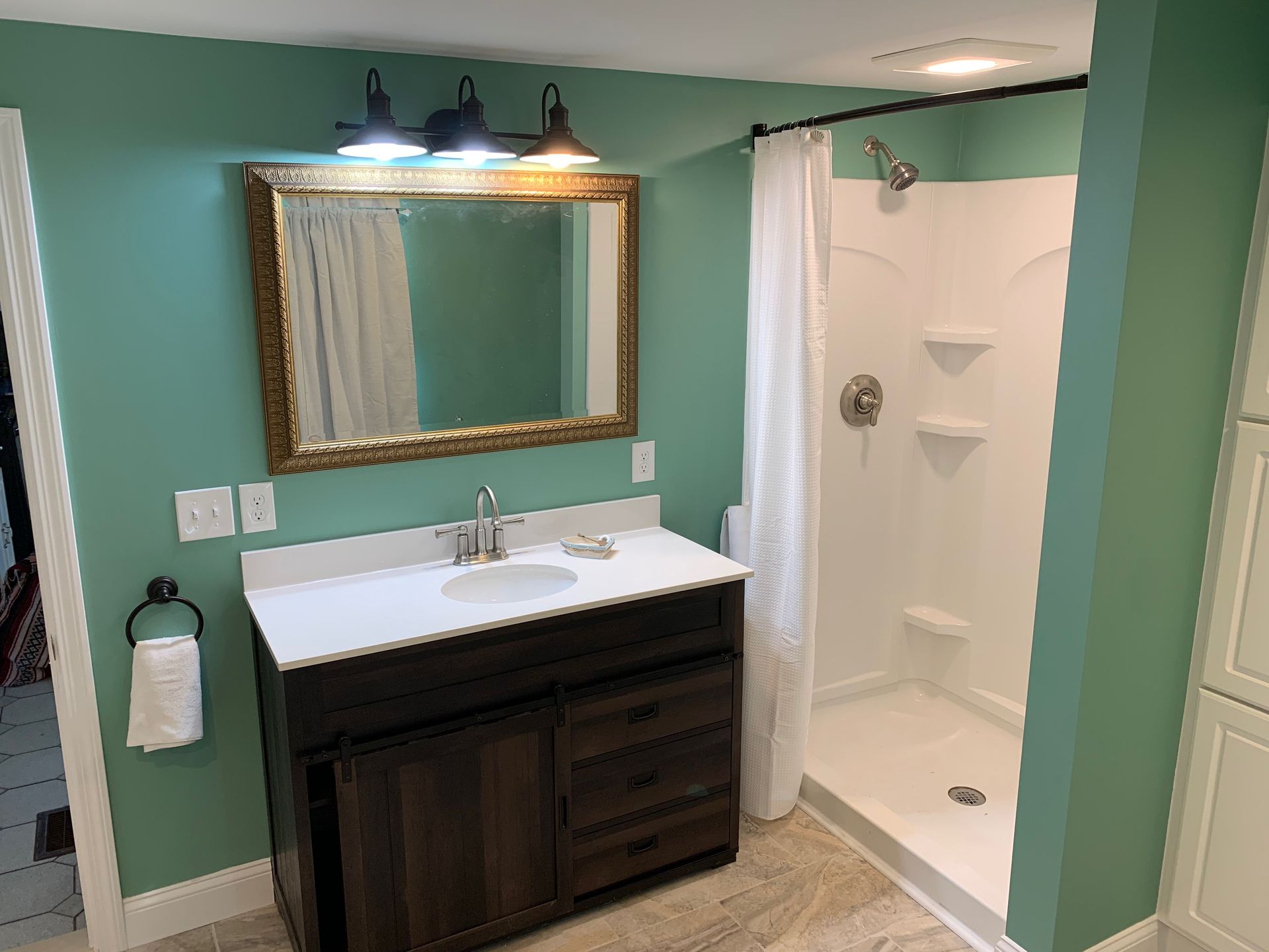 Bathroom with teal walls, dark wood vanity, white countertop, framed mirror, and shower.