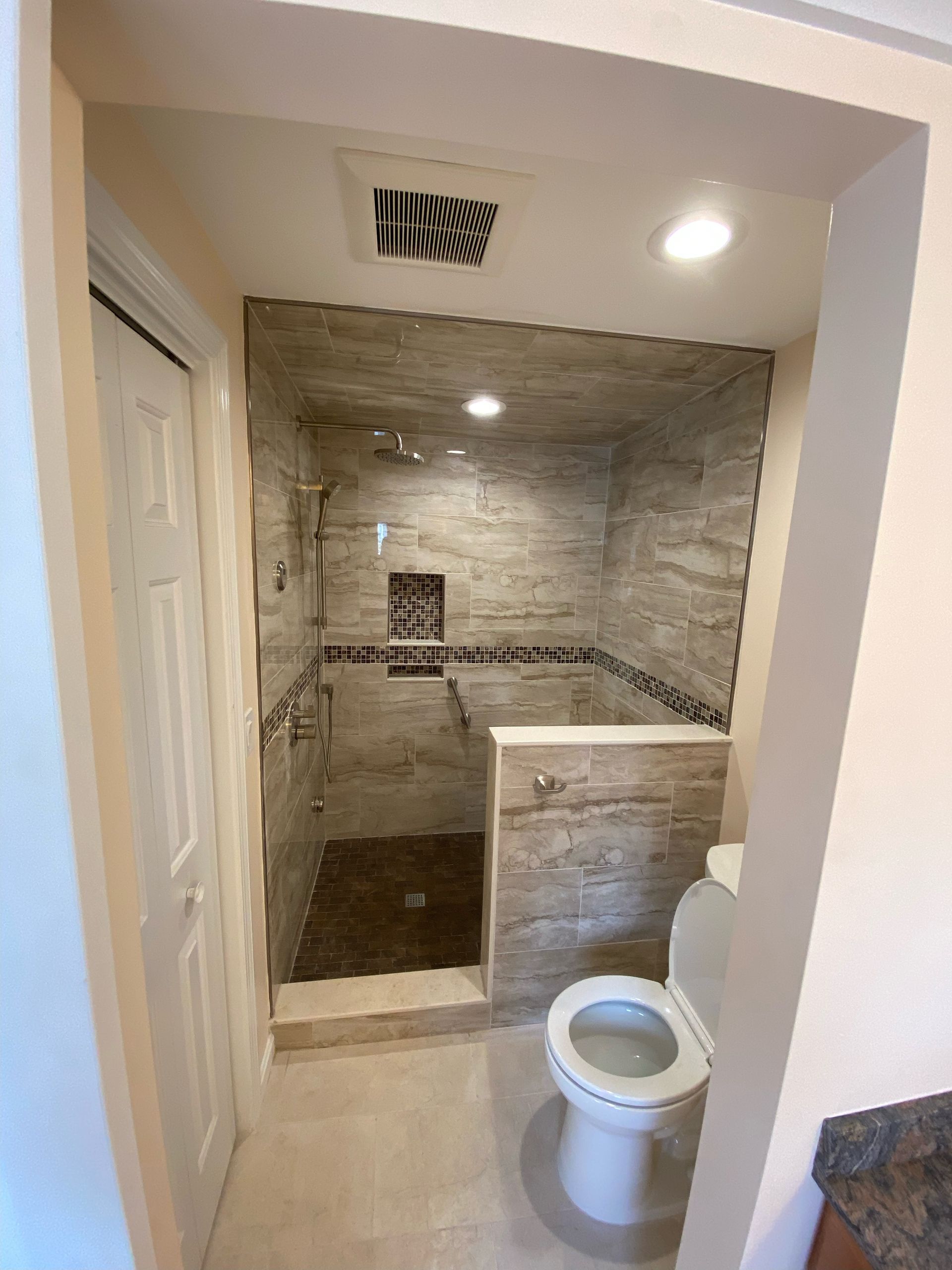 Bathroom with tile shower, toilet, and doorway. Beige and gray color scheme.