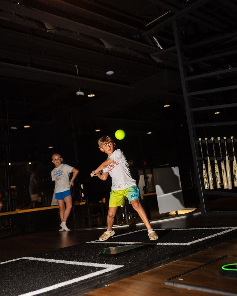 Two people playing indoor paddle tennis, with one mid-swing and a ball in the air.