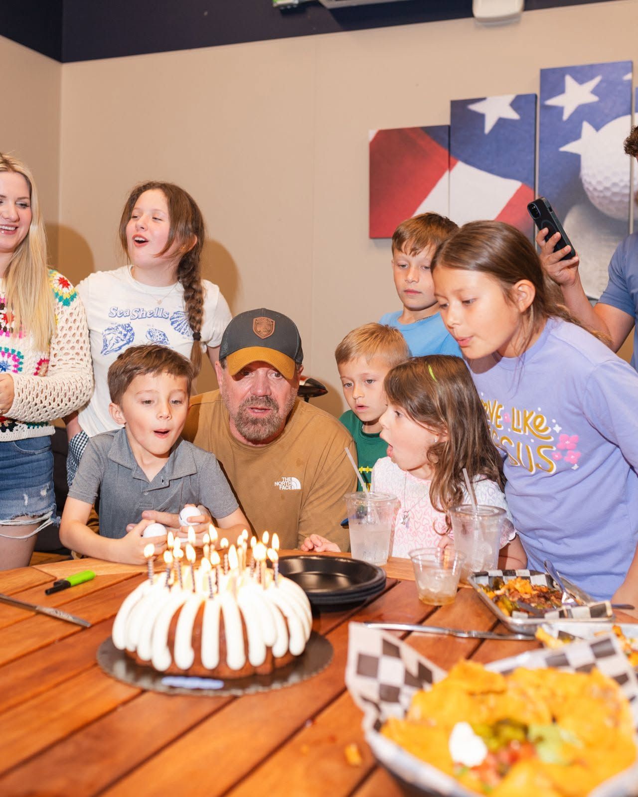 People gathered around a birthday cake with lit candles, smiling in a warmly lit dining room.