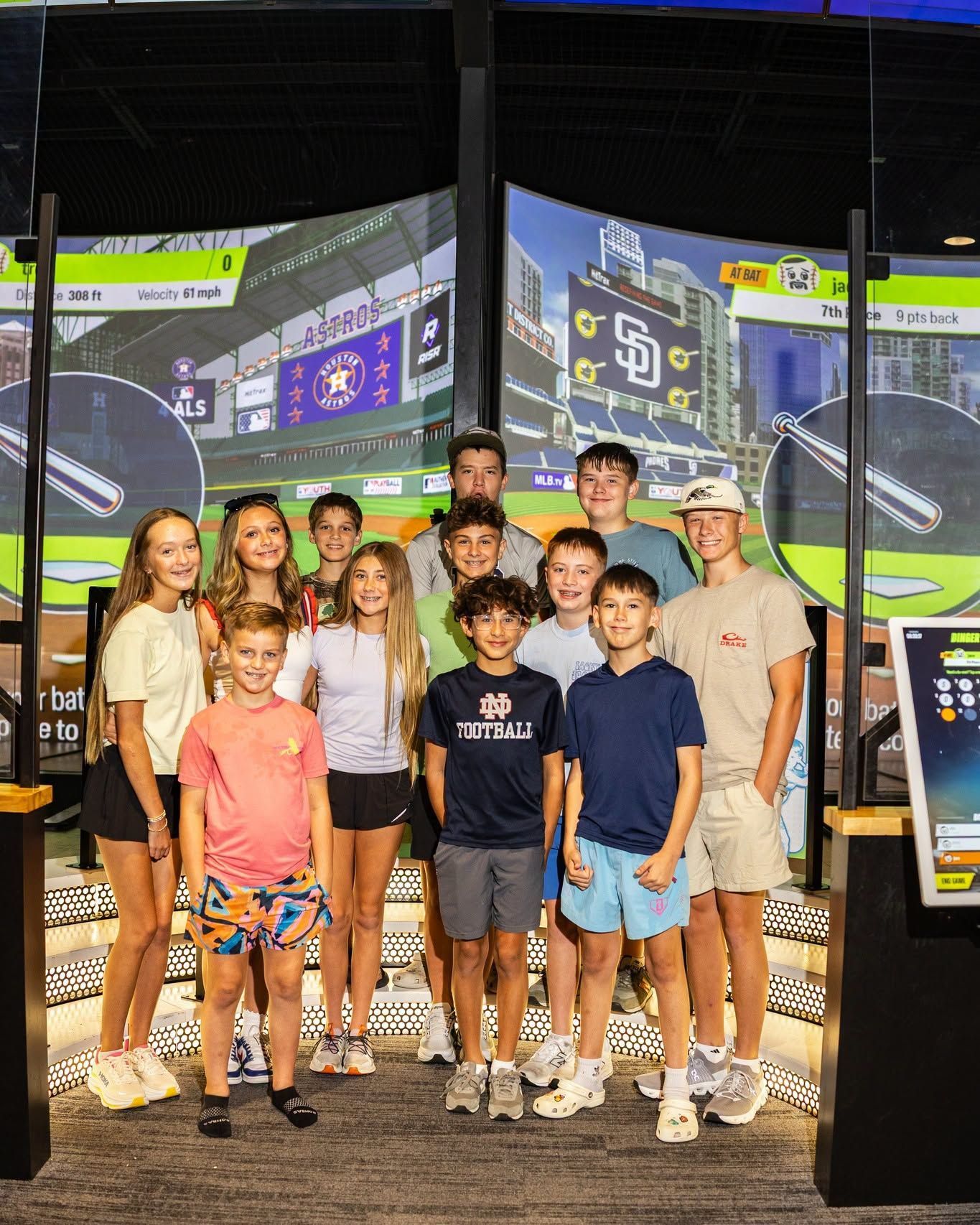 Group of people posing in front of arcade racing game screens, smiling at an indoor entertainment venue
